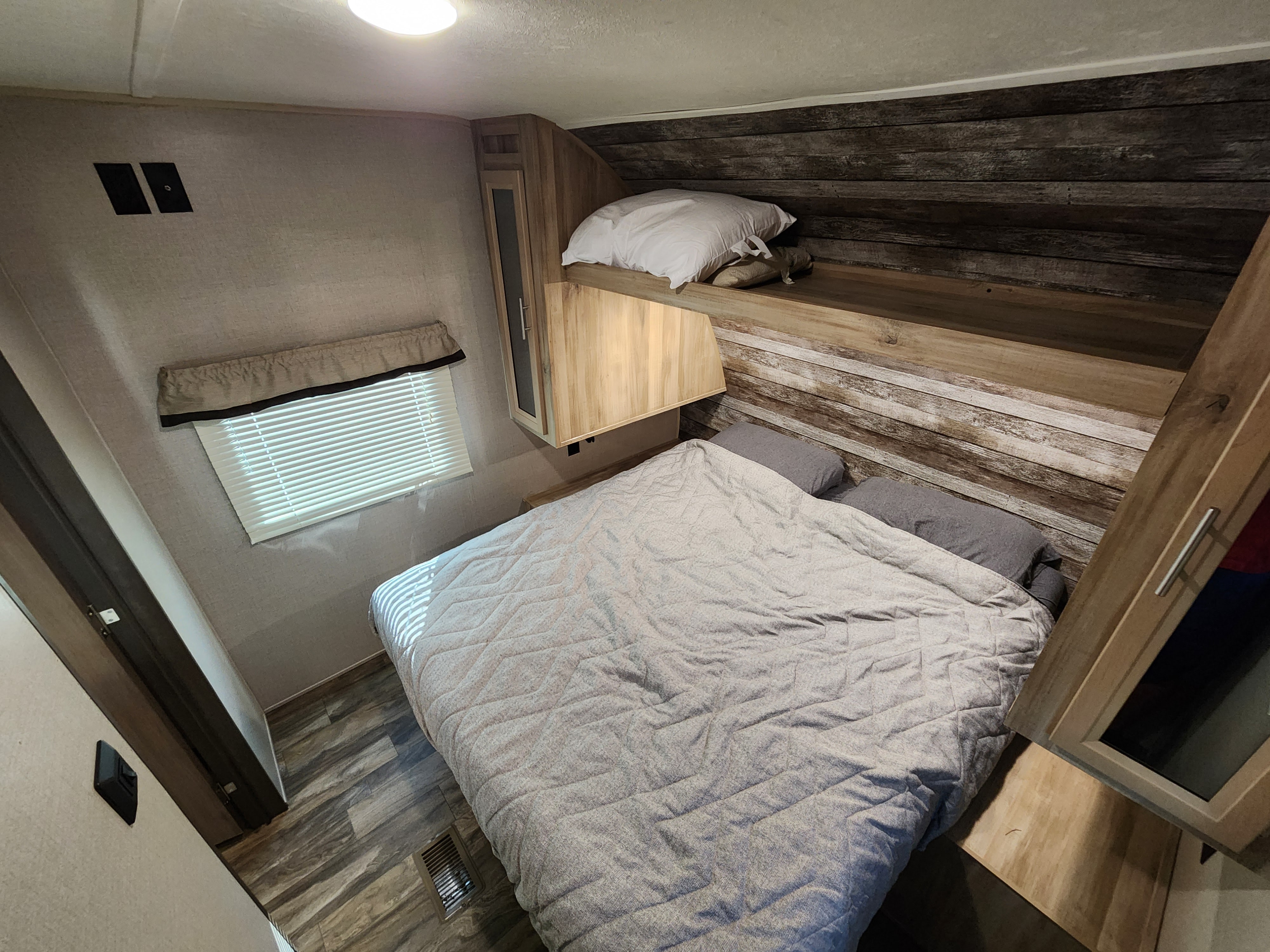 Cozy RV rental bedroom with wood accents, comfy bed, and window with blinds. Ideal for travel accommodation.. Forest River Coachmen Catalina Summit 2020