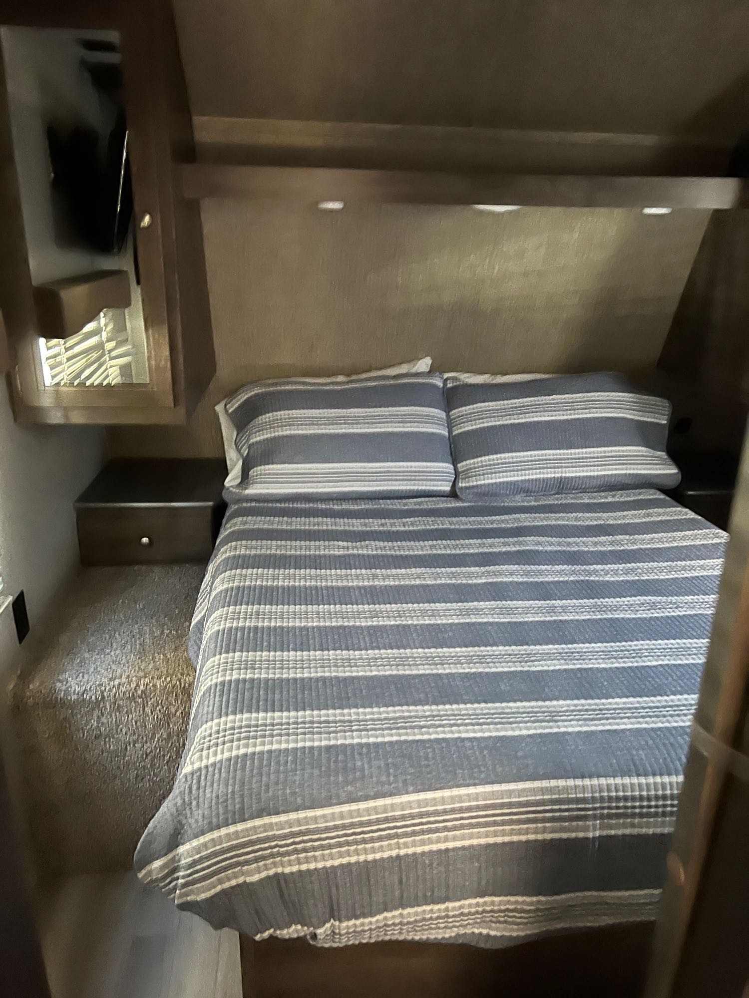 Comfortable RV rental bedroom with blue and white striped bedding, a nightstand, and overhead lights.. Keystone RV Coleman Lantern 2019