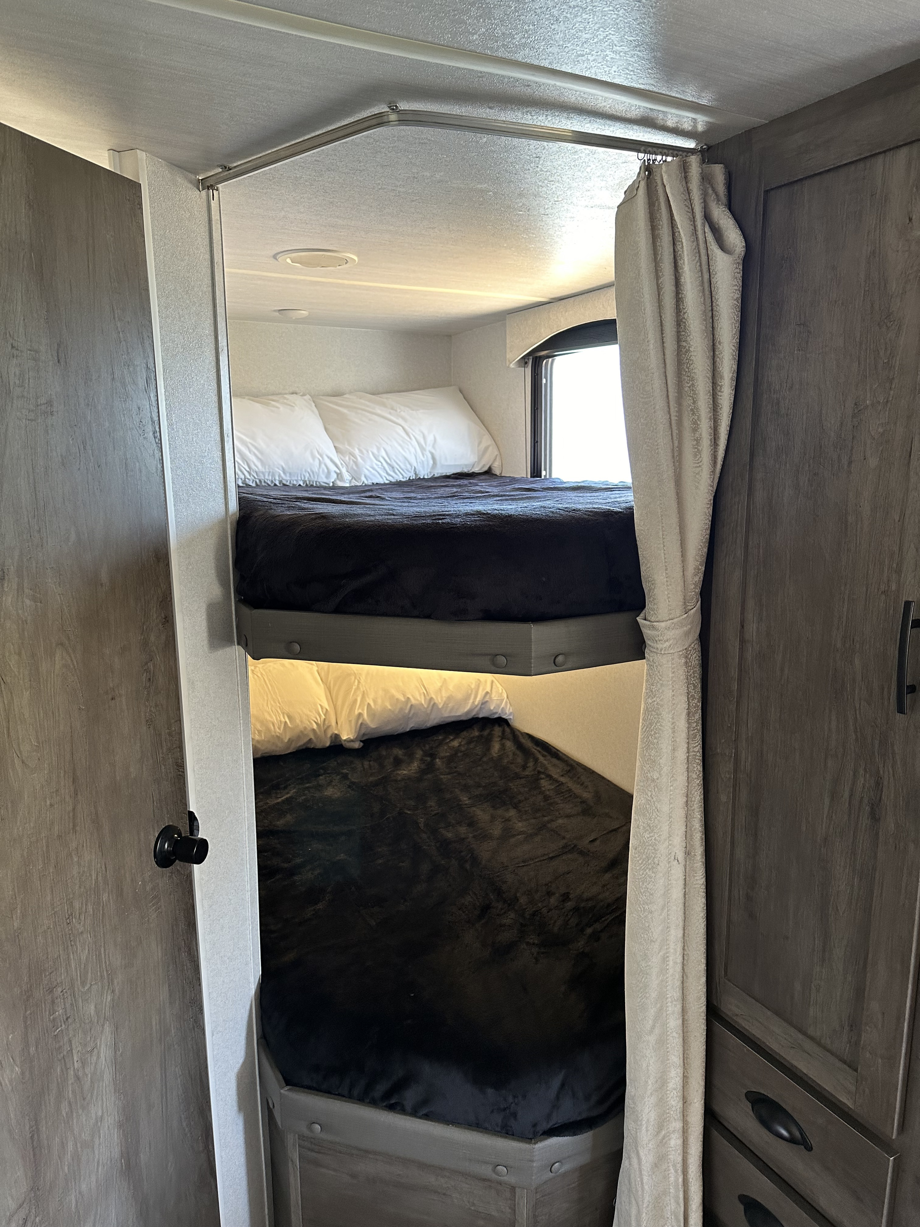 Cozy RV rental bunk beds with black blankets, privacy curtain, and a window for comfortable sleeping.. Forest River T2490 2020