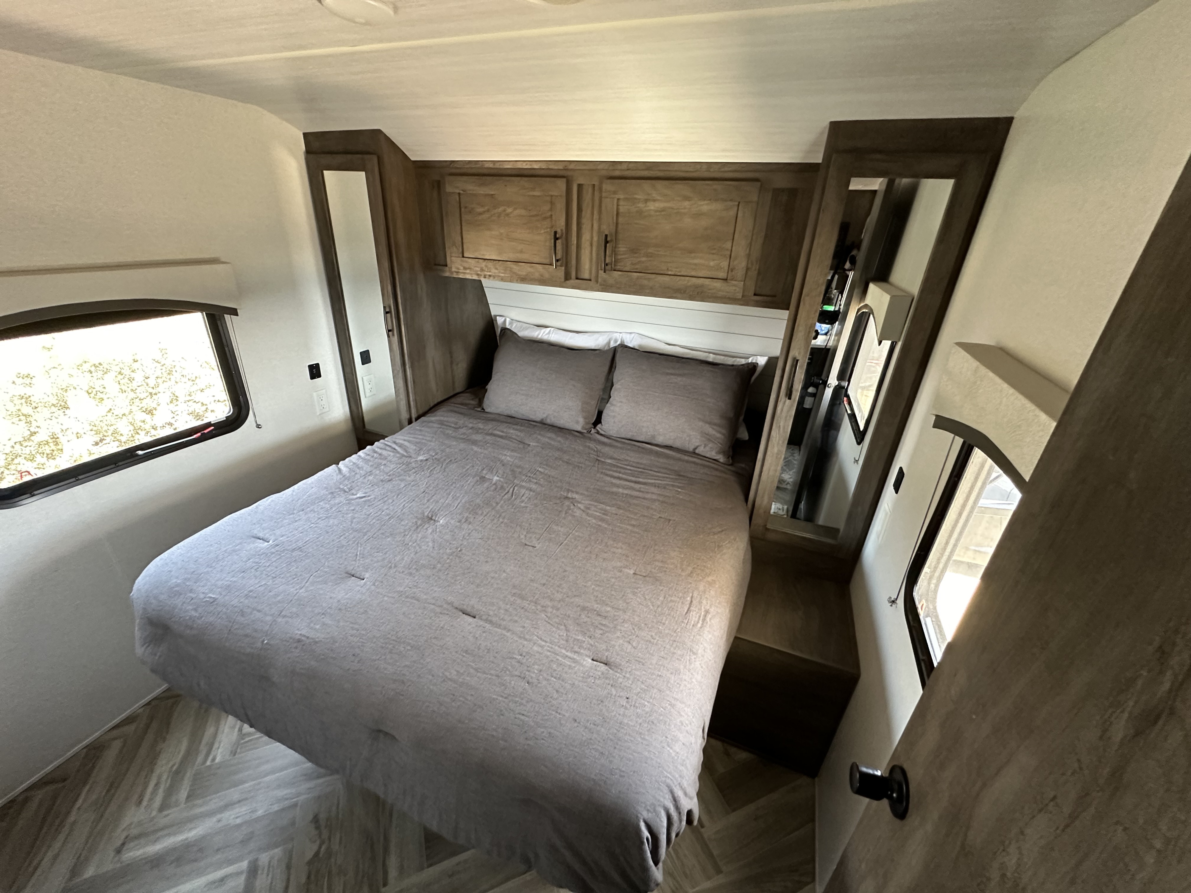 Cozy RV rental bedroom with a large bed, wood cabinets, mirrored wardrobes, and a bright window.. Forest River T2490 2020