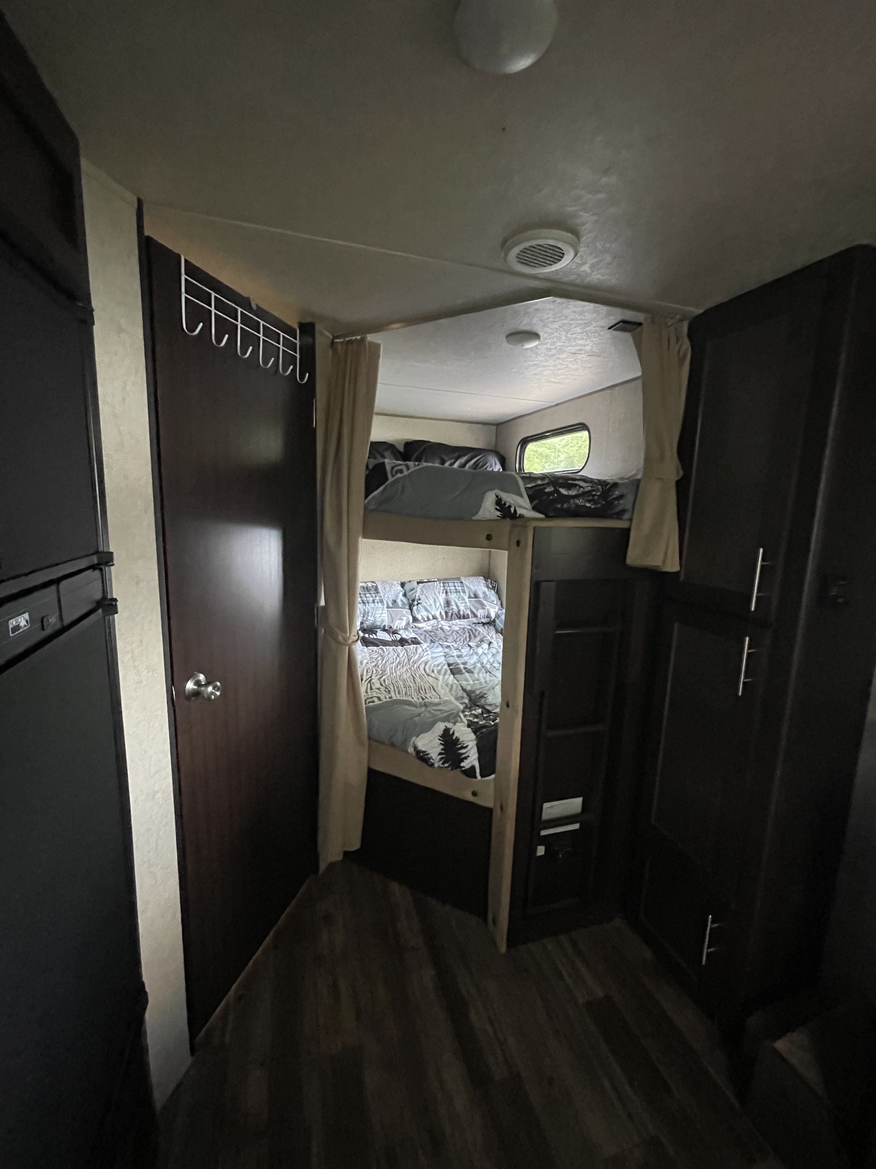 RV rental interior with cozy bunk beds, a door, and storage units, typical of a compact mobile living space.. Forest River Cherokee Grey Wolf 2016