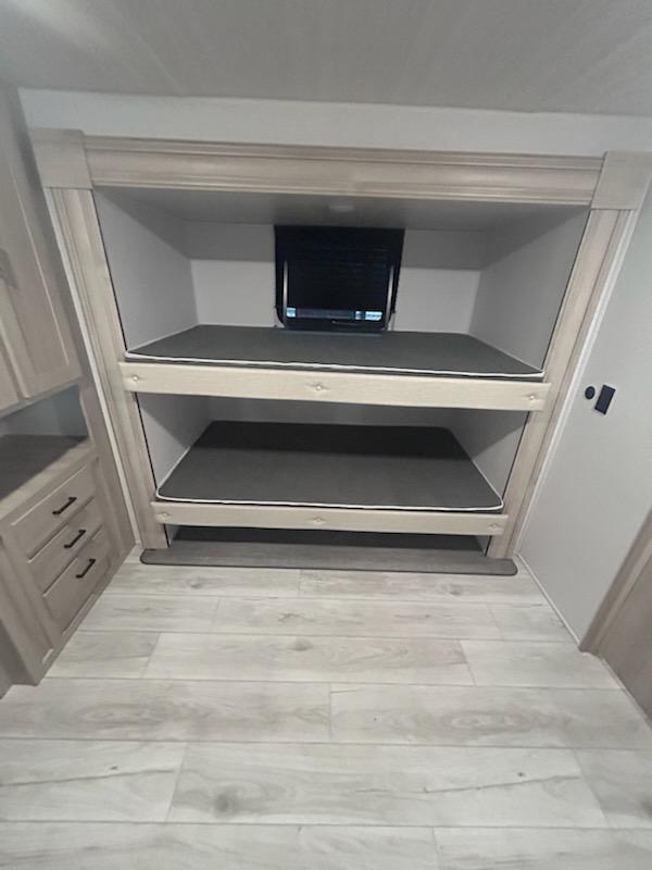 Cozy RV rental interior features stacked bunk beds with dark mattresses, light wood trim, and wood-look flooring.. East to West Della Terra LE 2024