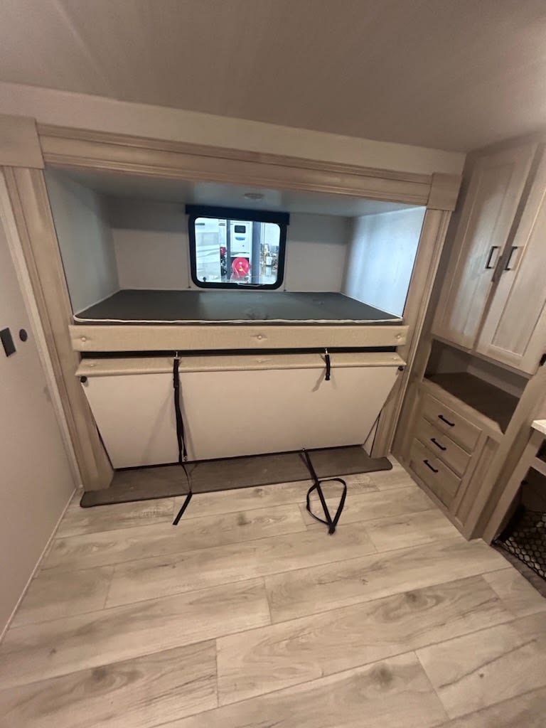 RV rental bunk area: Top bunk visible, bottom bunk folded & secured. Light wood floor & cabinets. Window shows outside.. East to West Della Terra LE 2024