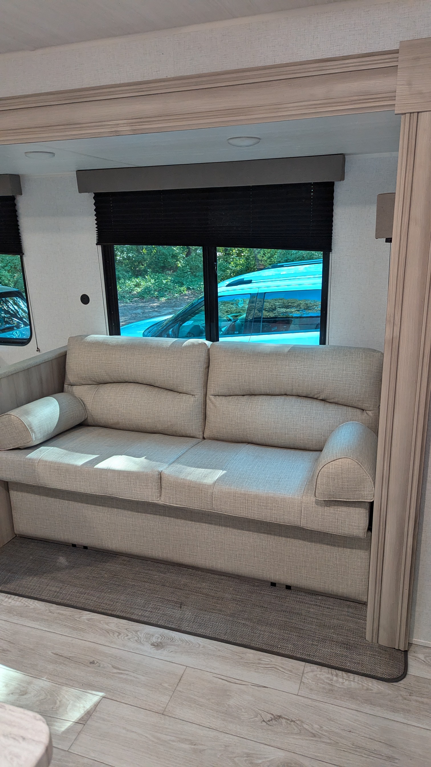 Cozy RV rental living space: light gray sofa, windows with dark blinds, wood-look floor, and a rug.. East to West Della Terra LE 2024