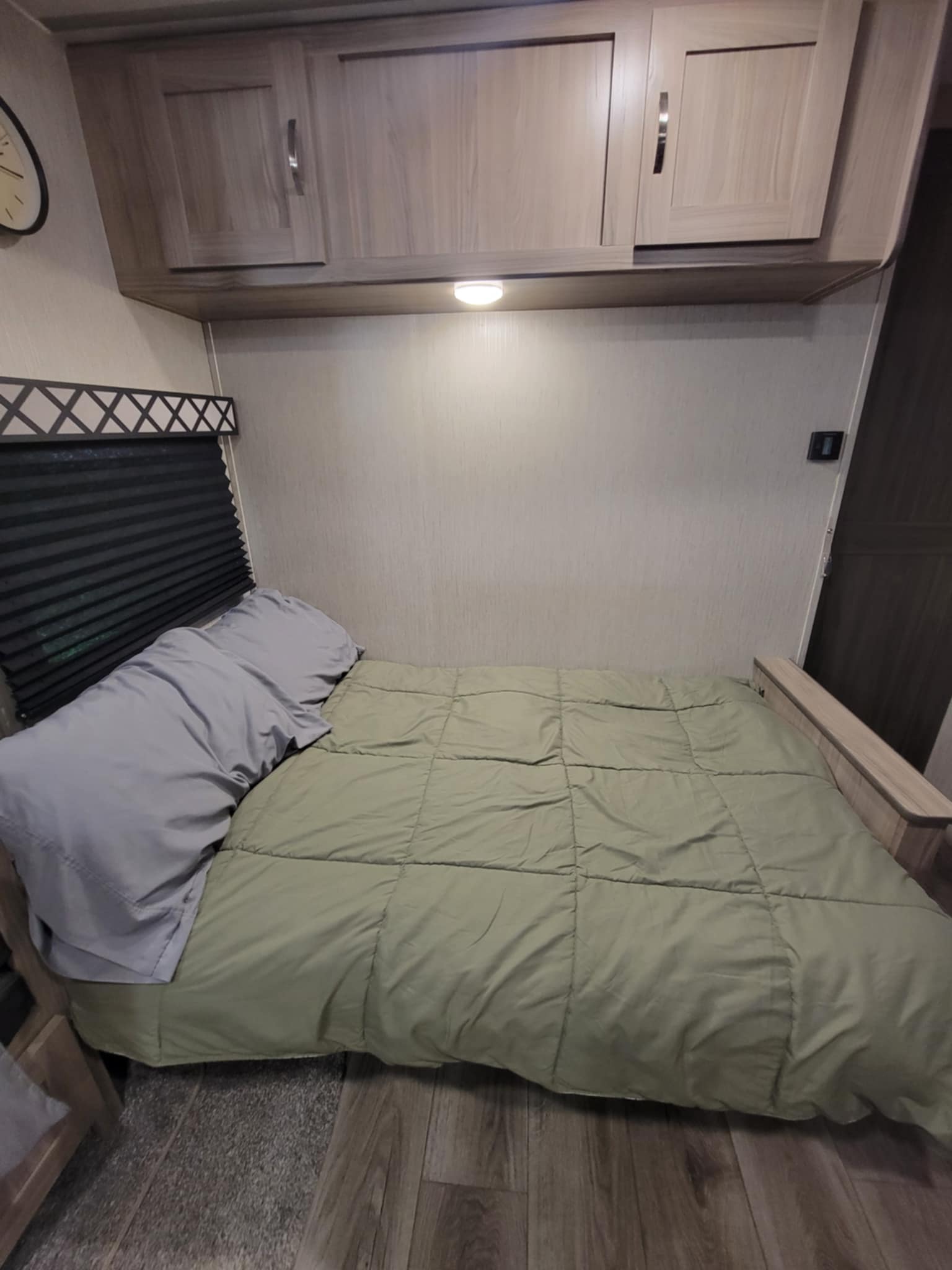 Cozy RV rental sleeping area featuring a bed with a green comforter, grey pillows, and overhead wood cabinets.. Coachmen Freedom Express 248RBS 2020