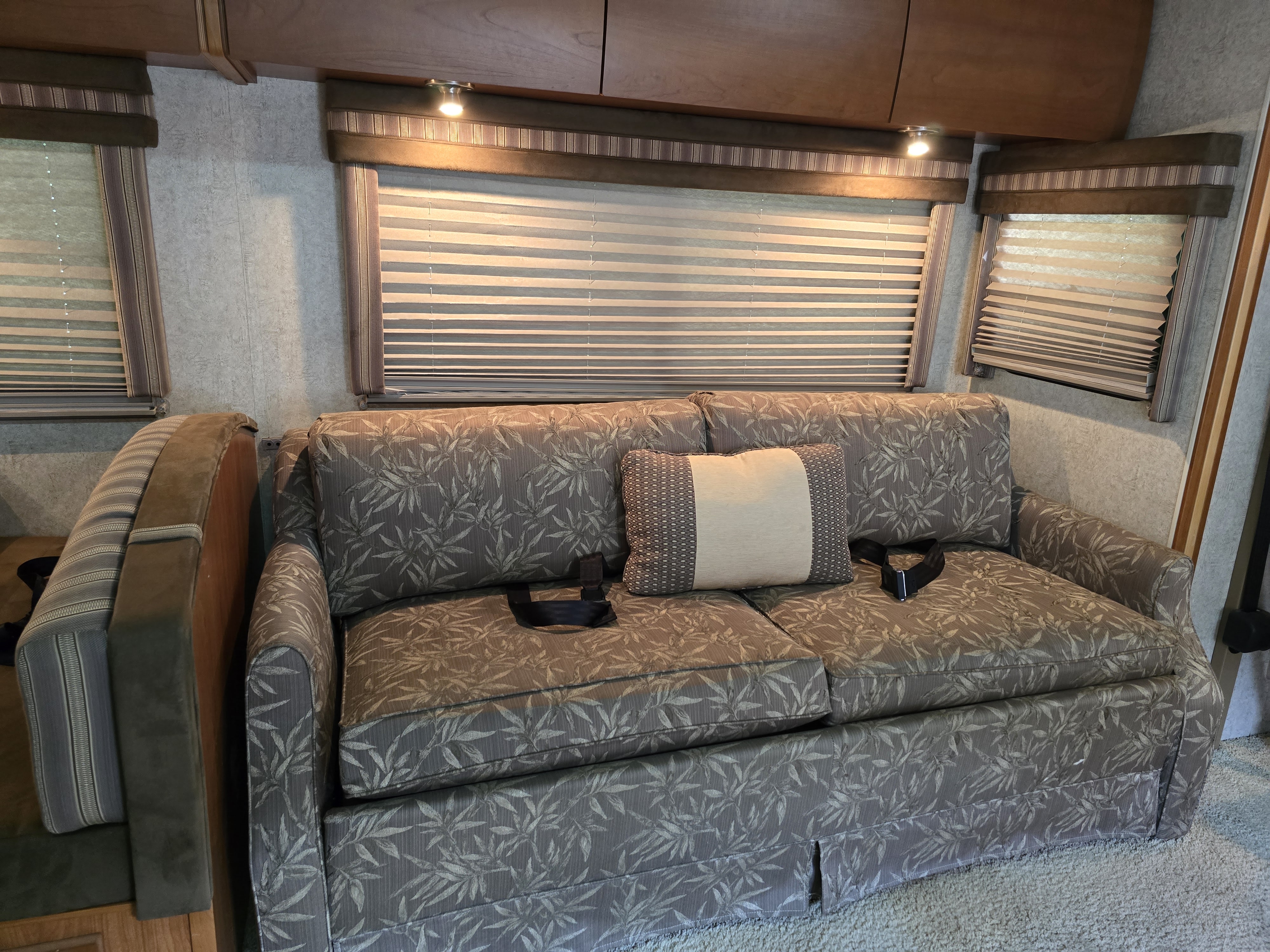 RV rental interior: a patterned sofa with seatbelts, a decorative pillow, and windows with blinds and overhead lights.. Winnebago Sightseer 2008