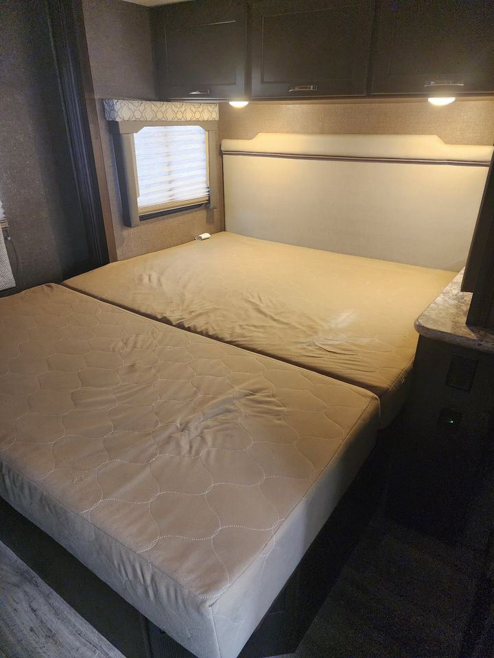 Inside an RV rental: Dual mattresses, upholstered headboard, and overhead storage. A compact bedroom space.. Thor Freedom Elite 2019