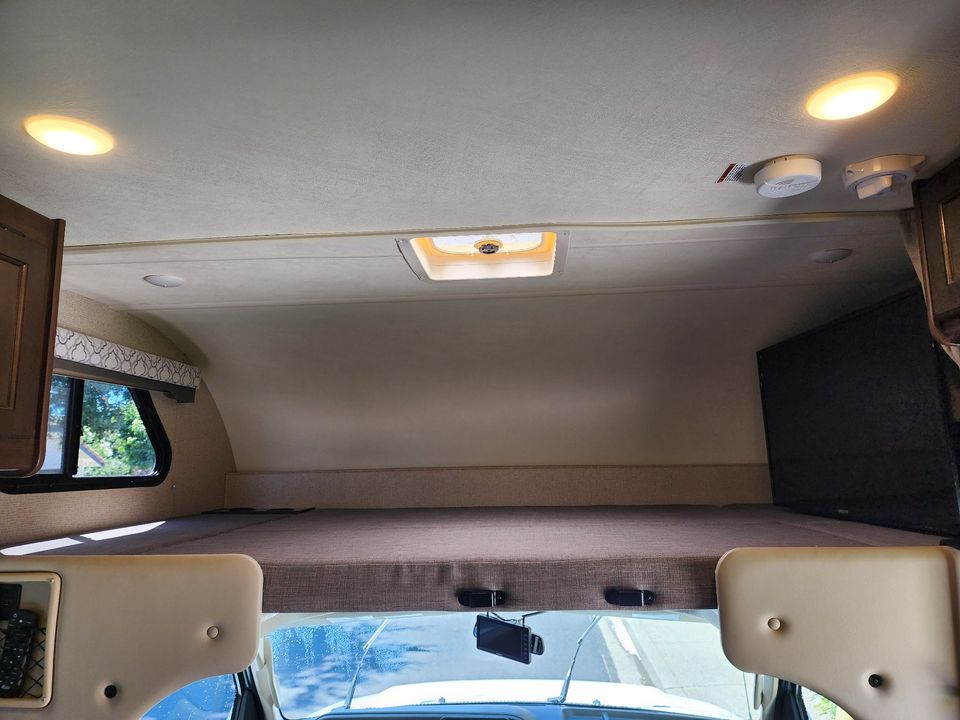 Inside an **RV rental**: cozy overhead bunk bed, ceiling lights, vent, window, and TV. Perfect for adventurous travel!. Thor Freedom Elite 2019