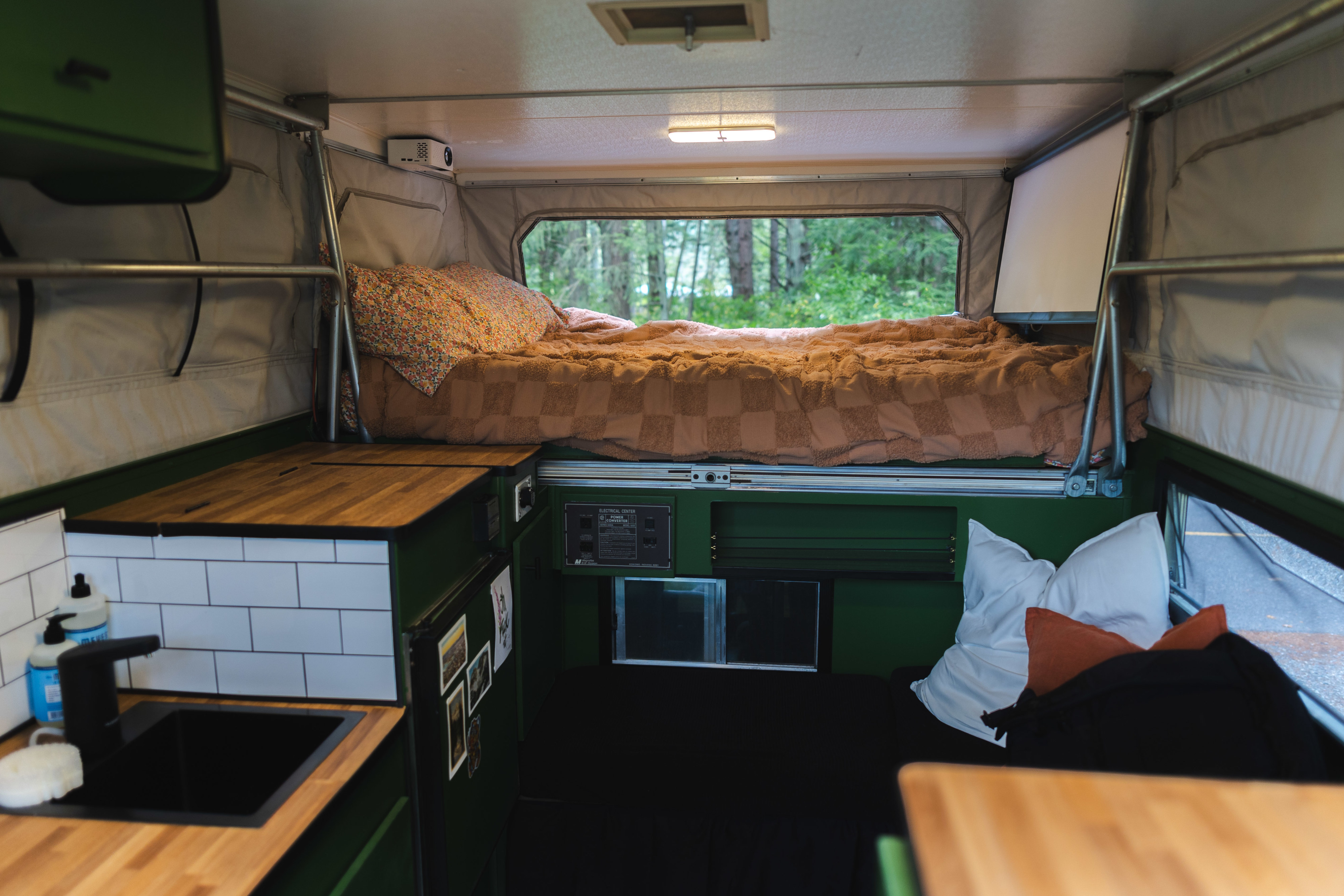 Inside a unique rv rental: cozy elevated bed, kitchen with sink, projector, & forest views.. Starcraft Sportstar 1991