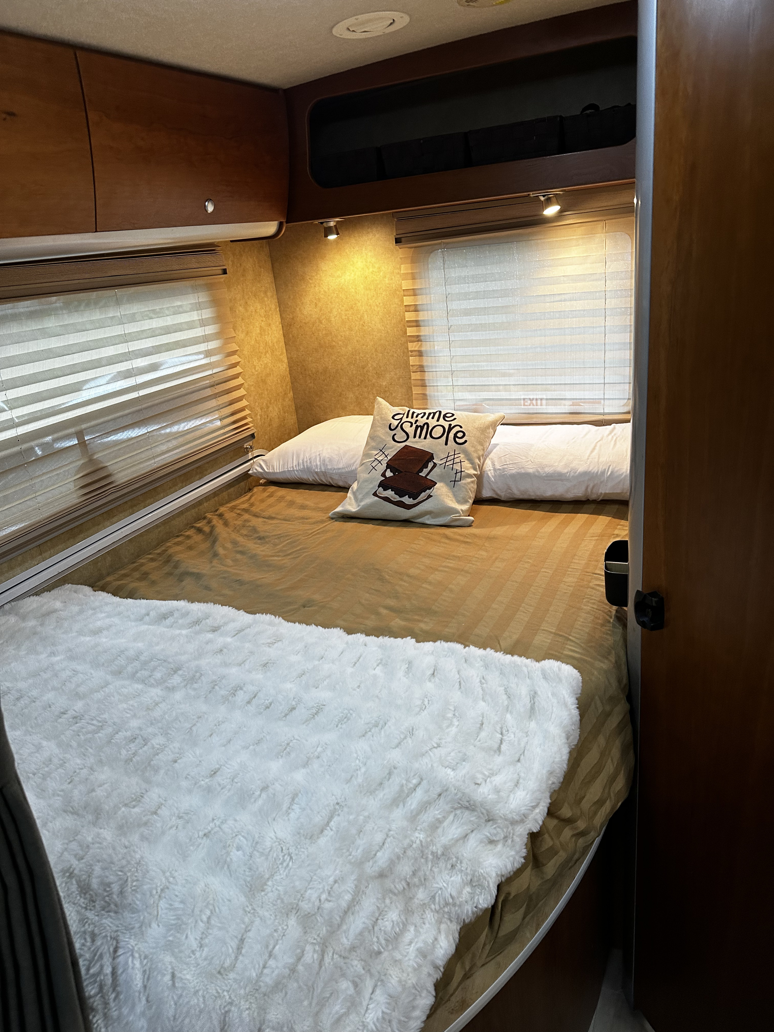 RV rental bedroom: a cozy bed with a brown striped comforter, white fluffy blanket, and a "Gimme S'more" pillow.. Winnebago Itasca 2007