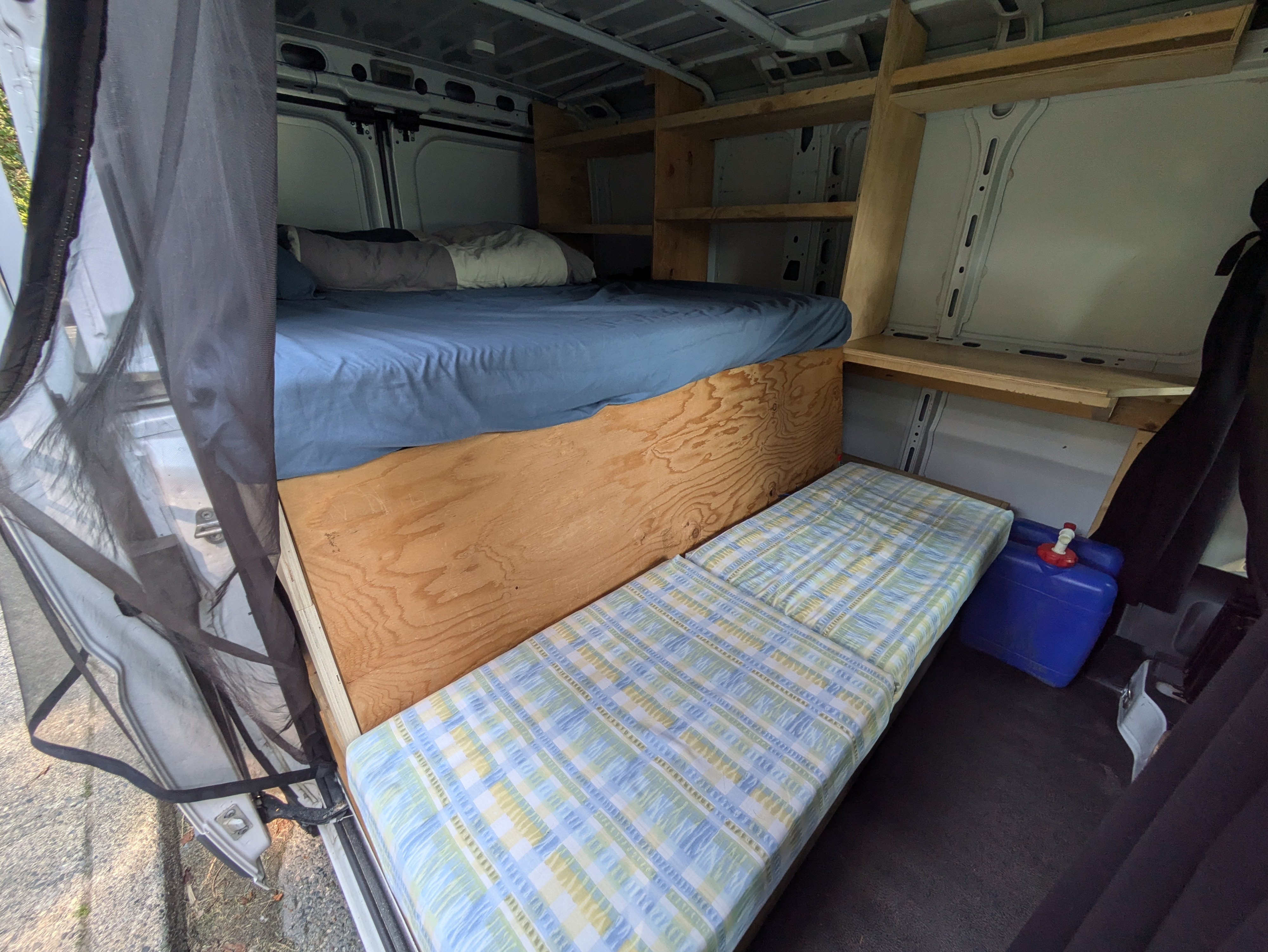 Cozy camper van interior with elevated main bed, lower daybed, custom shelving, and a water jug, perfect for an RV rental adventure.. Dodge Ram Promaster 2017