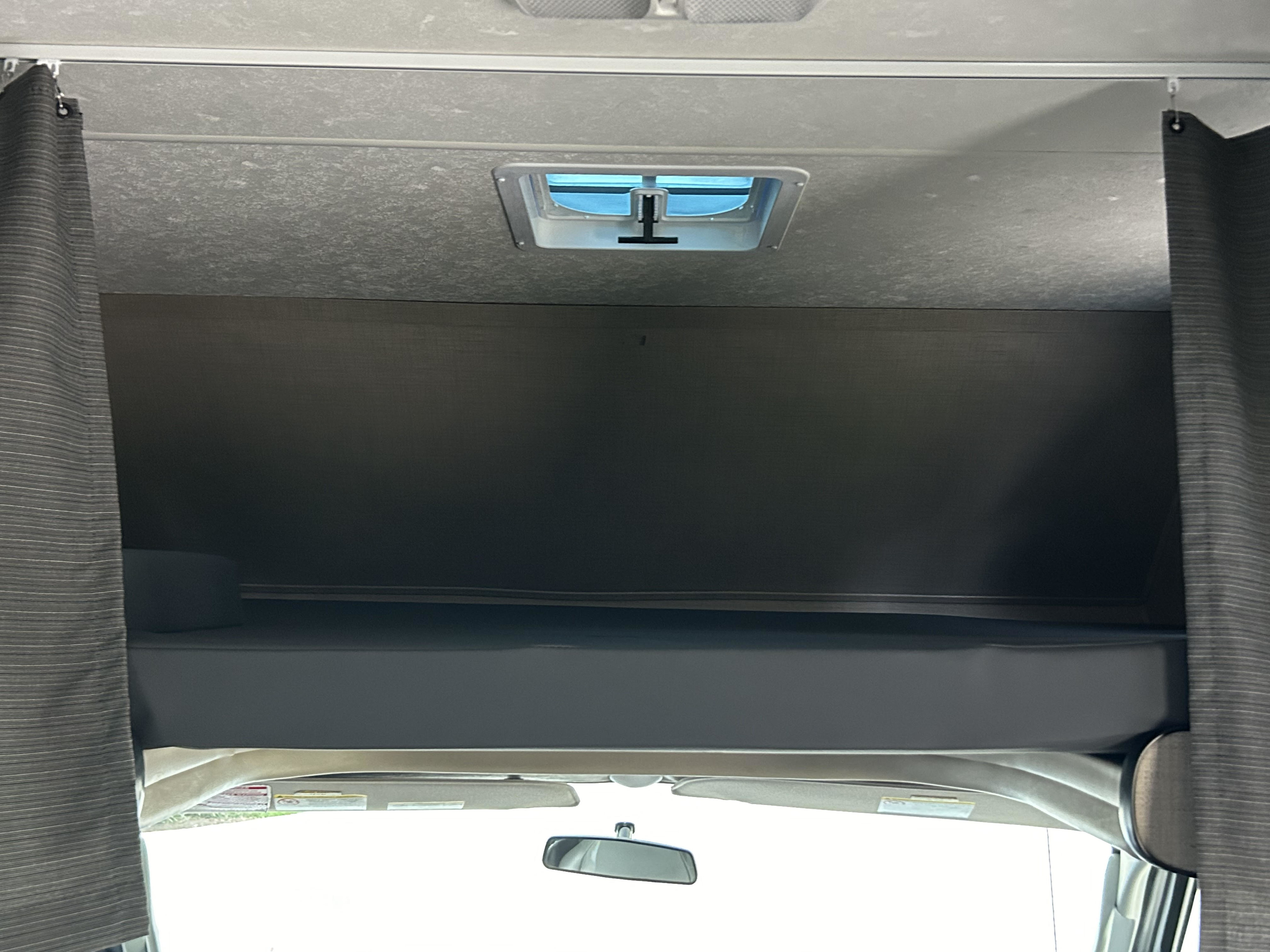 RV rental: Overhead view of a cab-over bunk with a grey mattress, ceiling vent, and privacy curtains.. Thor Majestic 2020