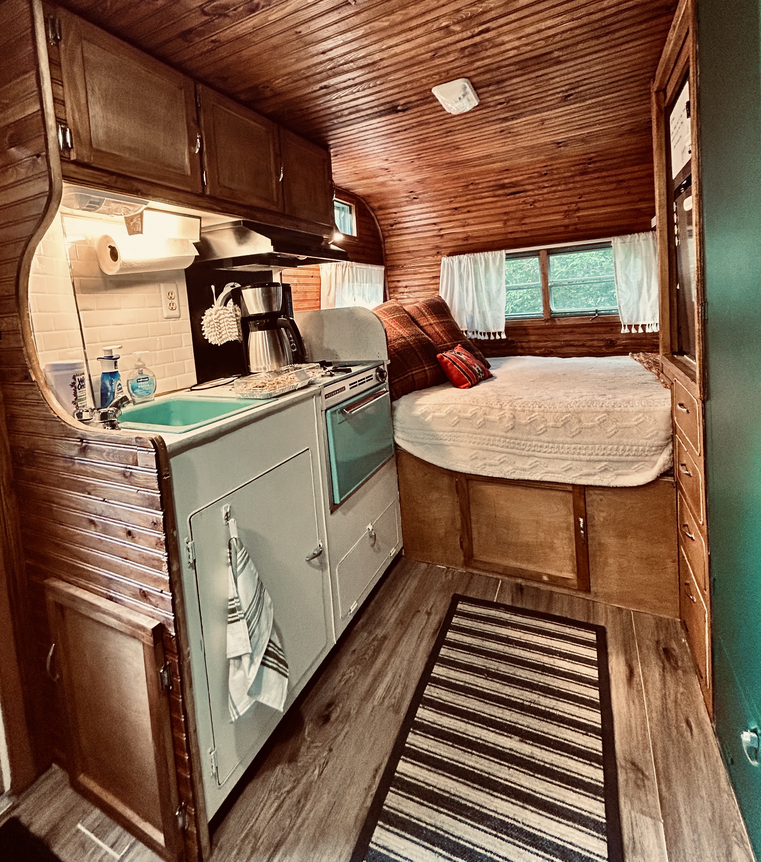 RV rental: Rustic RV interior with wood paneling, a compact kitchen featuring a light blue stove, and a comfortable bed area.. Skyline Nomad 1966