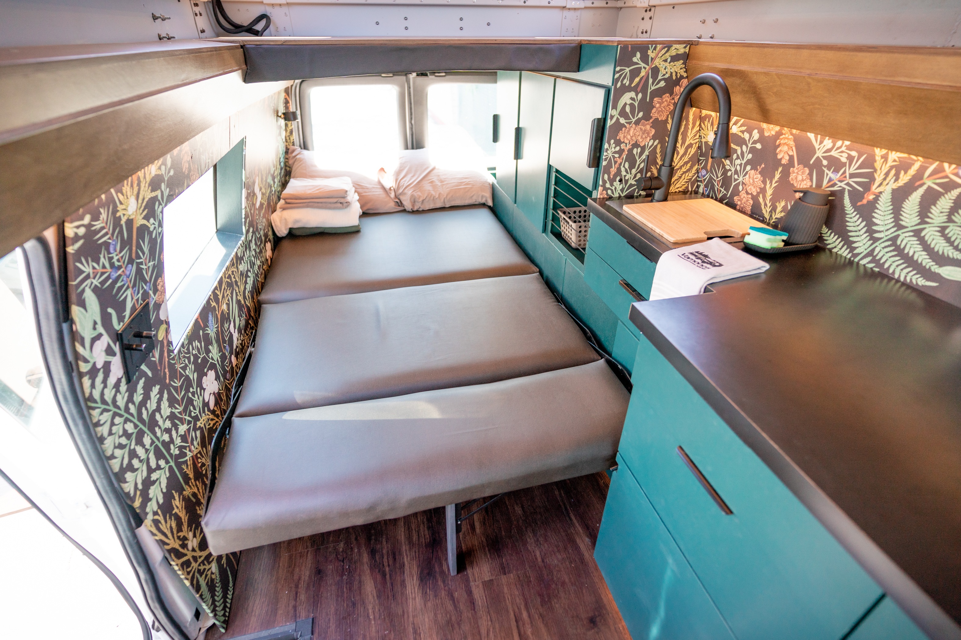 Compact RV rental interior: teal kitchen, floral walls, and versatile bed for travel comfort.. Ford Econoline 2008