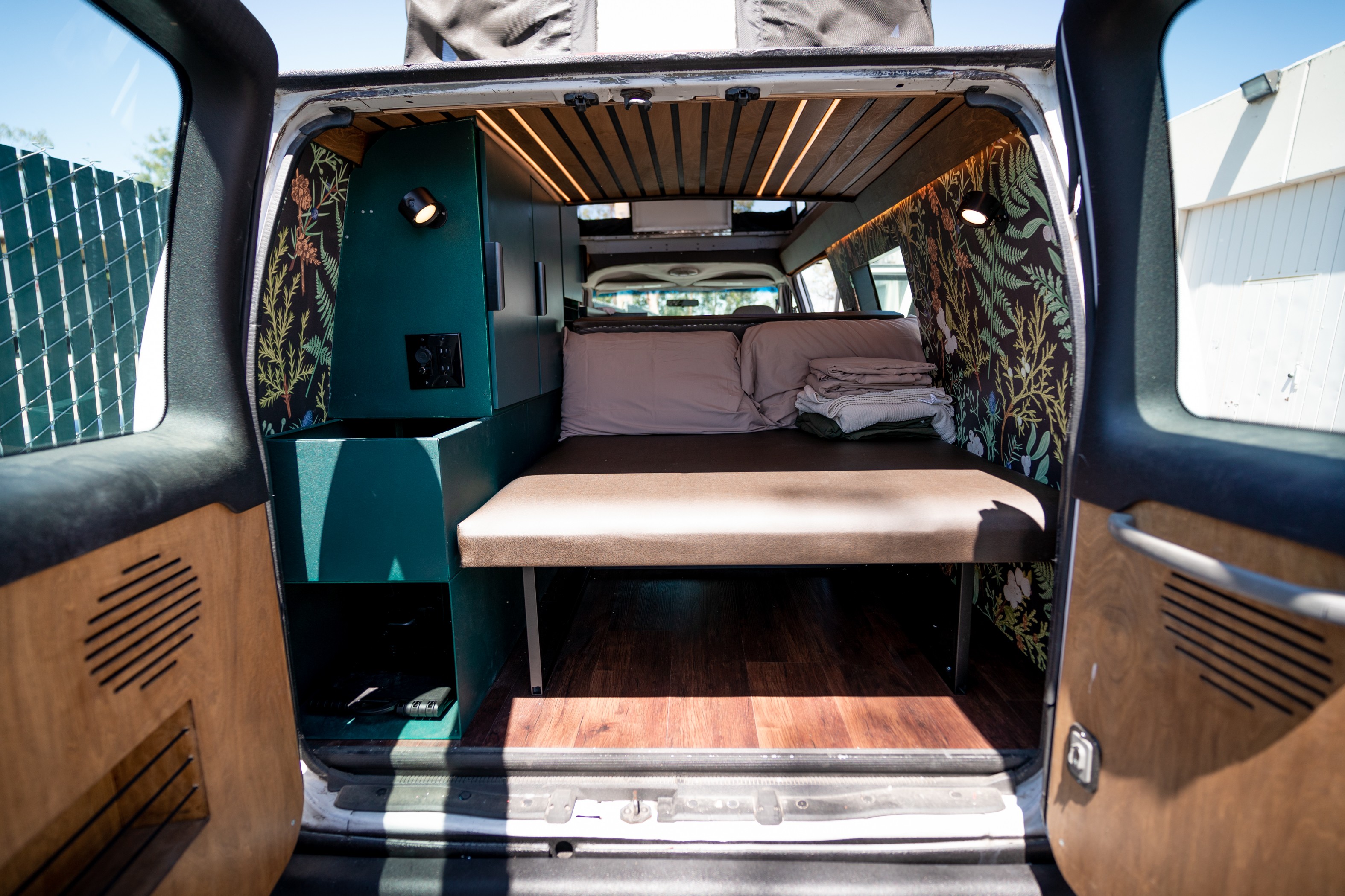 Spacious custom camper van interior perfect for an RV rental adventure, featuring a comfy bed, storage, wood accents, and floral wallpaper.. Ford Econoline 2008