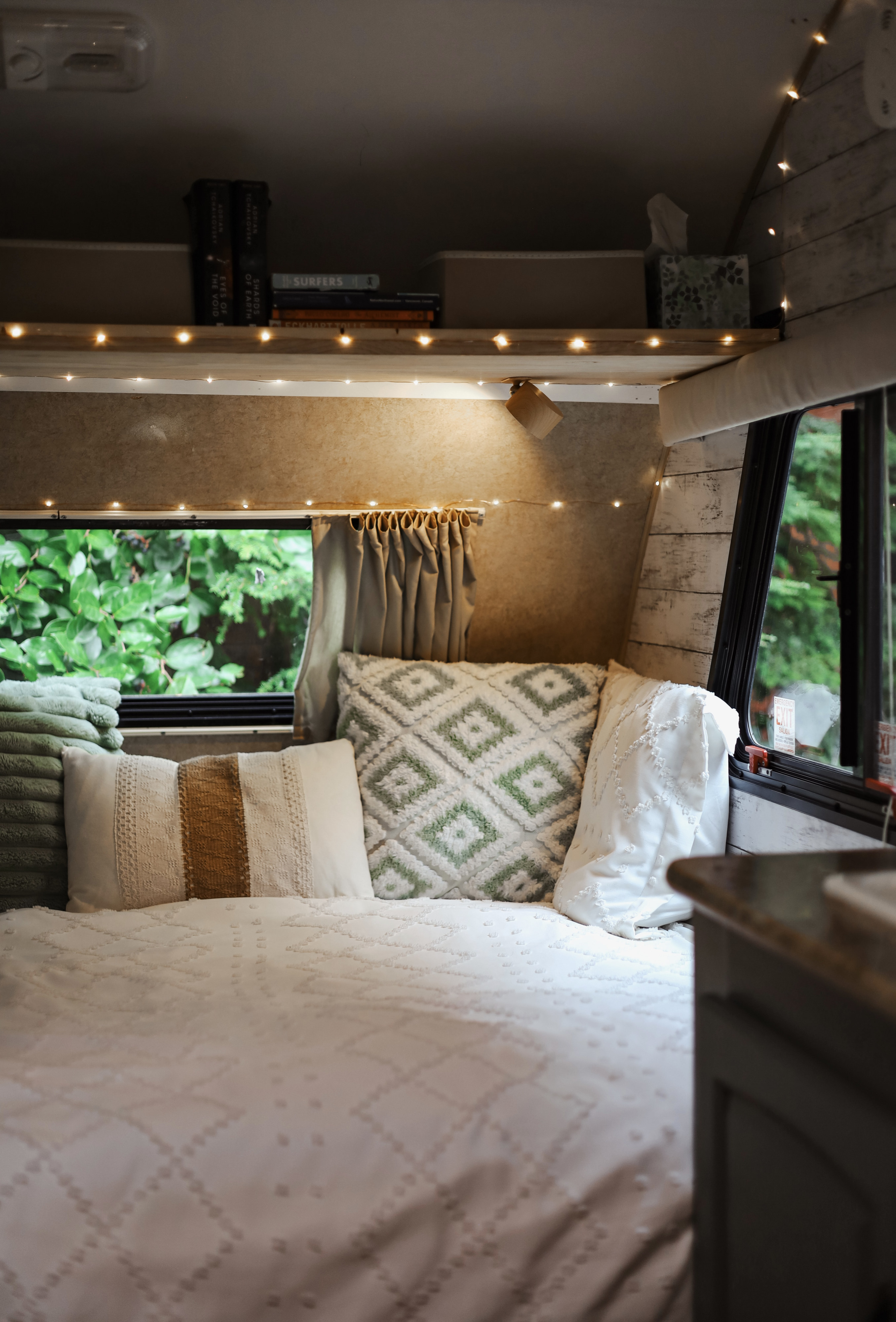 Cozy rv rental bedroom features soft bed, decorative pillows, string lights, and books. Green view from this peaceful camper.. R-Pod R-Pod Trailer 2012
