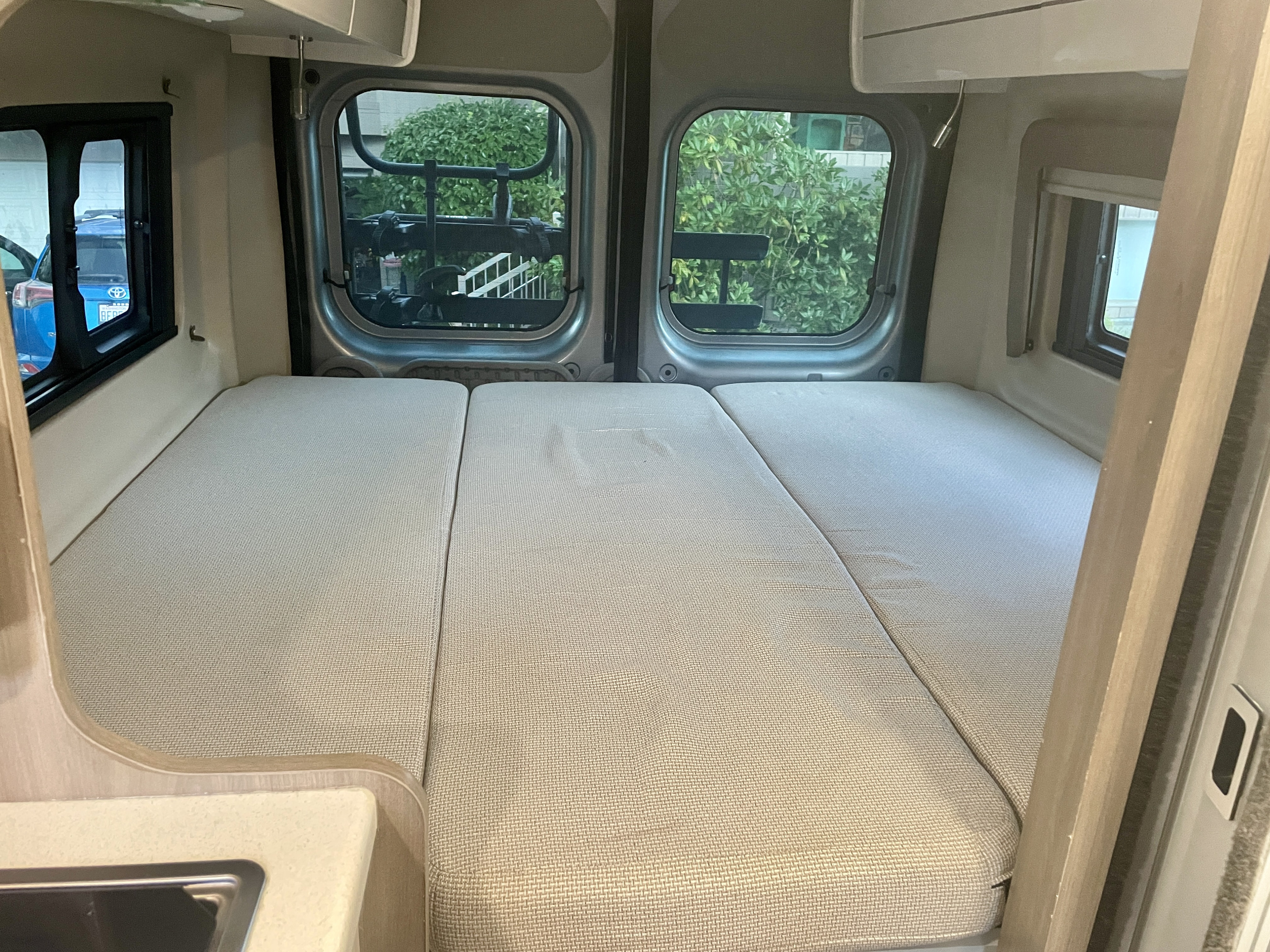 Inside a cozy rv rental: A modular bed with three segments, large windows, and a small sink area visible.. Thor Tellaro 2022