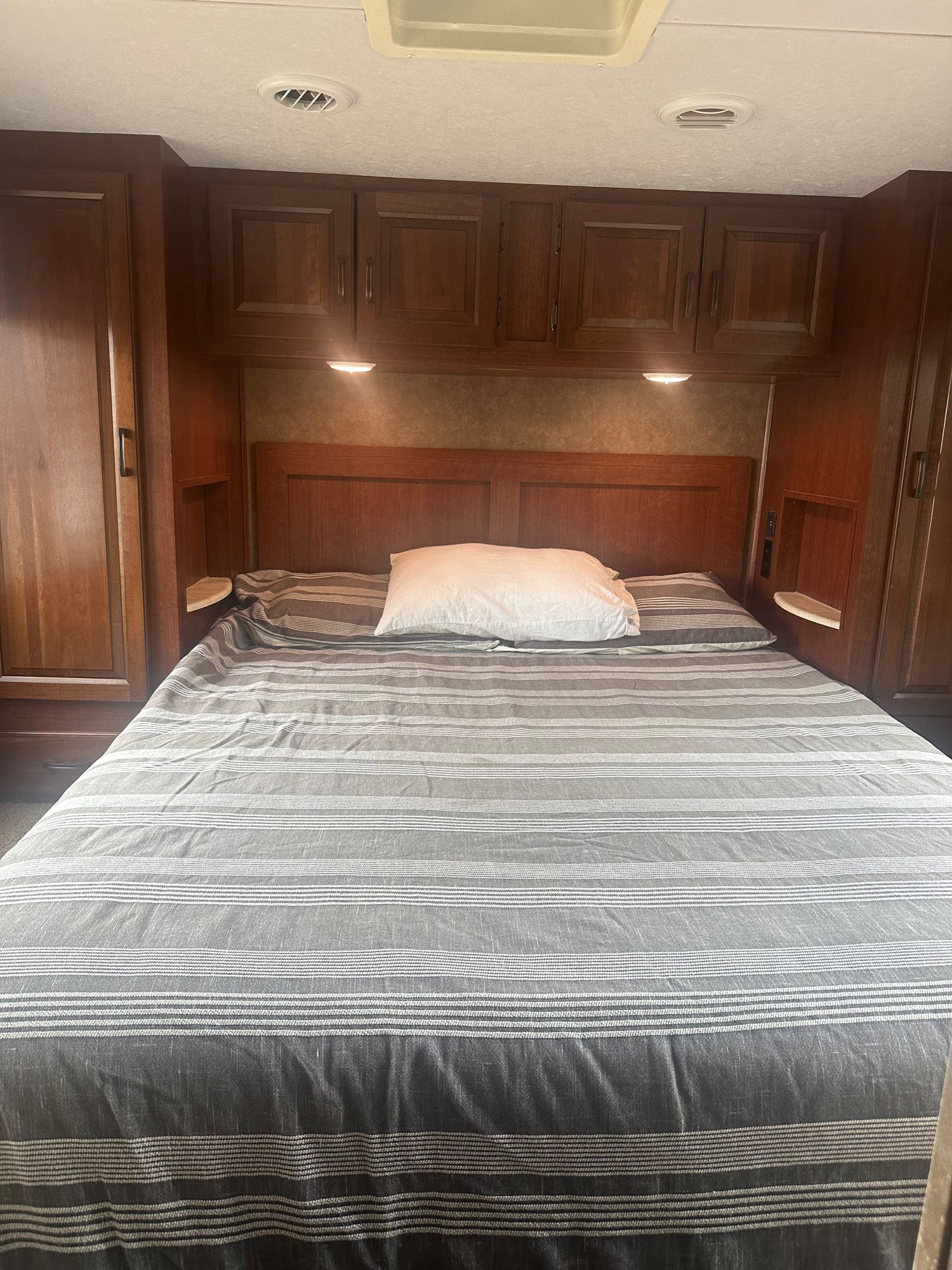 Cozy RV rental bedroom with striped bedding, wood cabinets, and built-in storage.. Forest River Sunseeker 2016