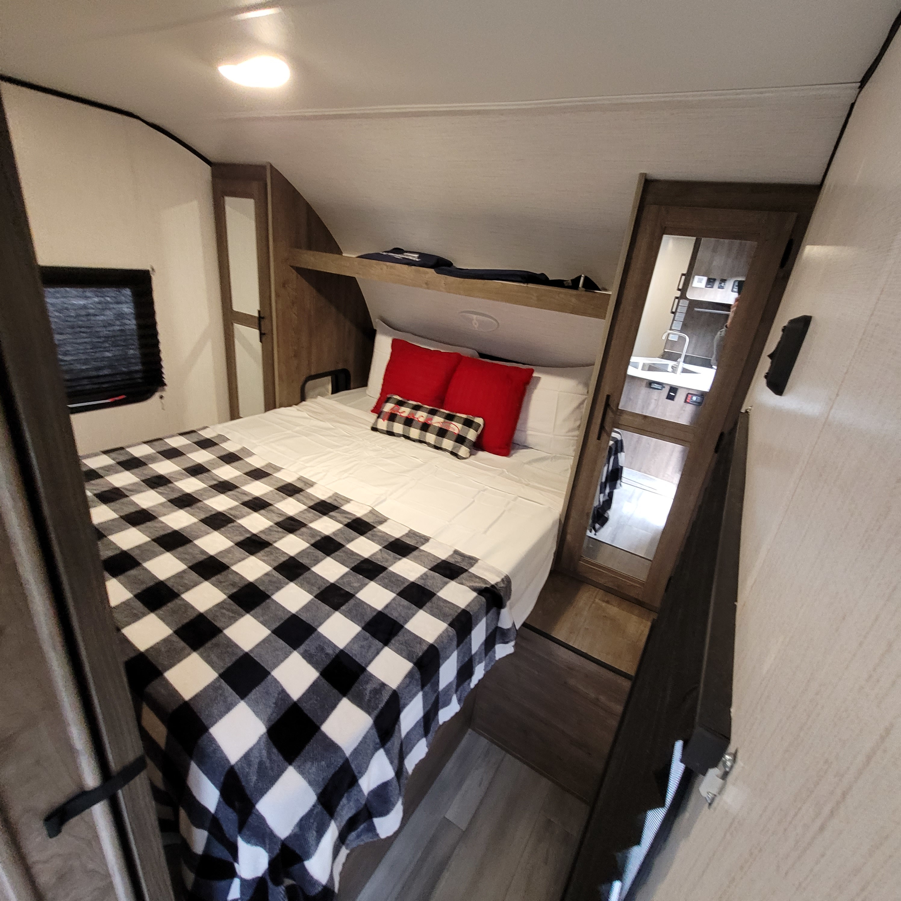 Cozy RV rental bedroom with buffalo plaid decor, a bed, and a mirrored door reflecting the kitchen area.. Heartland RVs Pioneer 2022