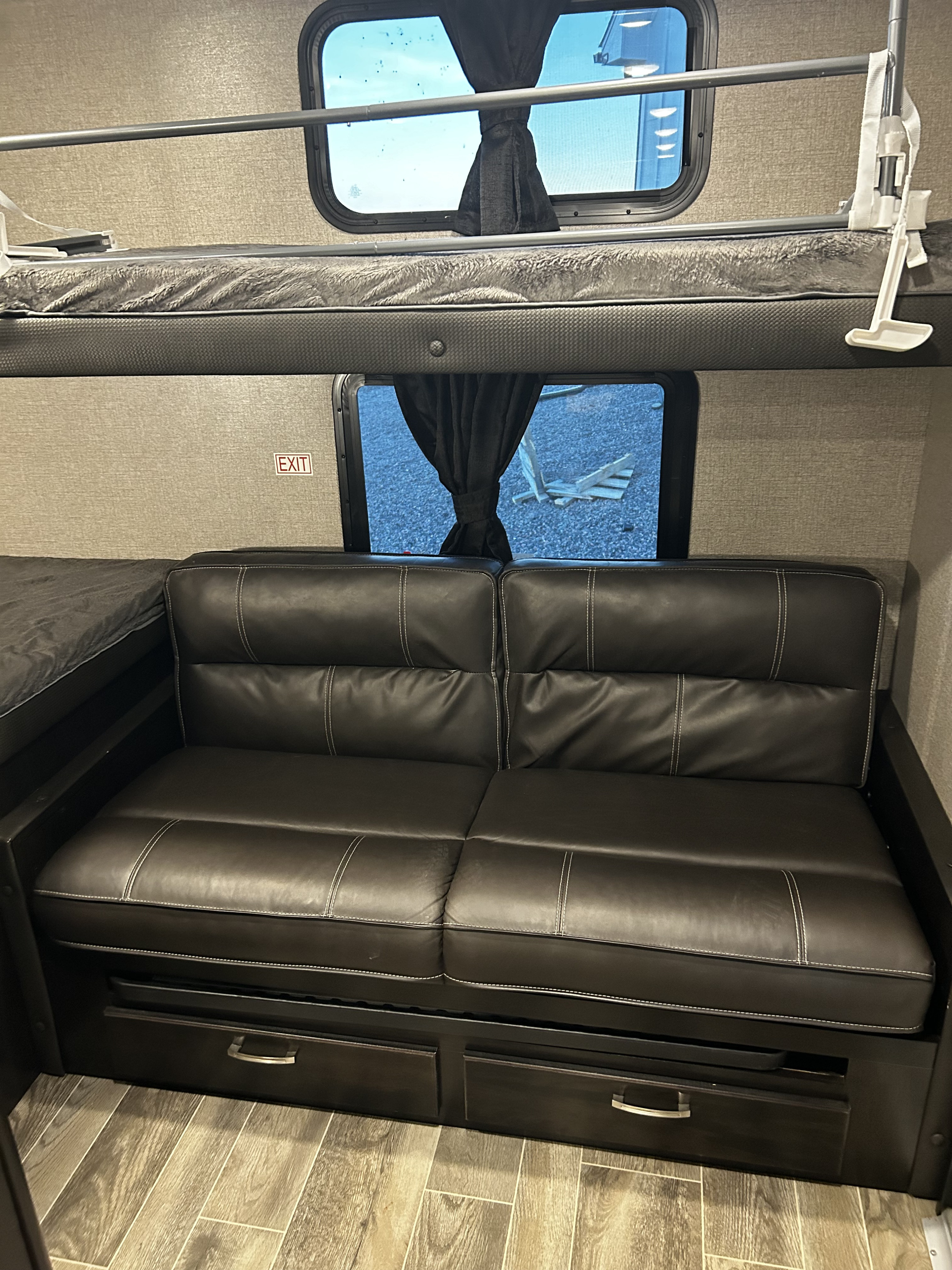 RV rental interior features an upper bunk bed, black sofa with under-sofa storage, and large windows. An 'EXIT' sign is visible.. Jayco Jay Feather 2021