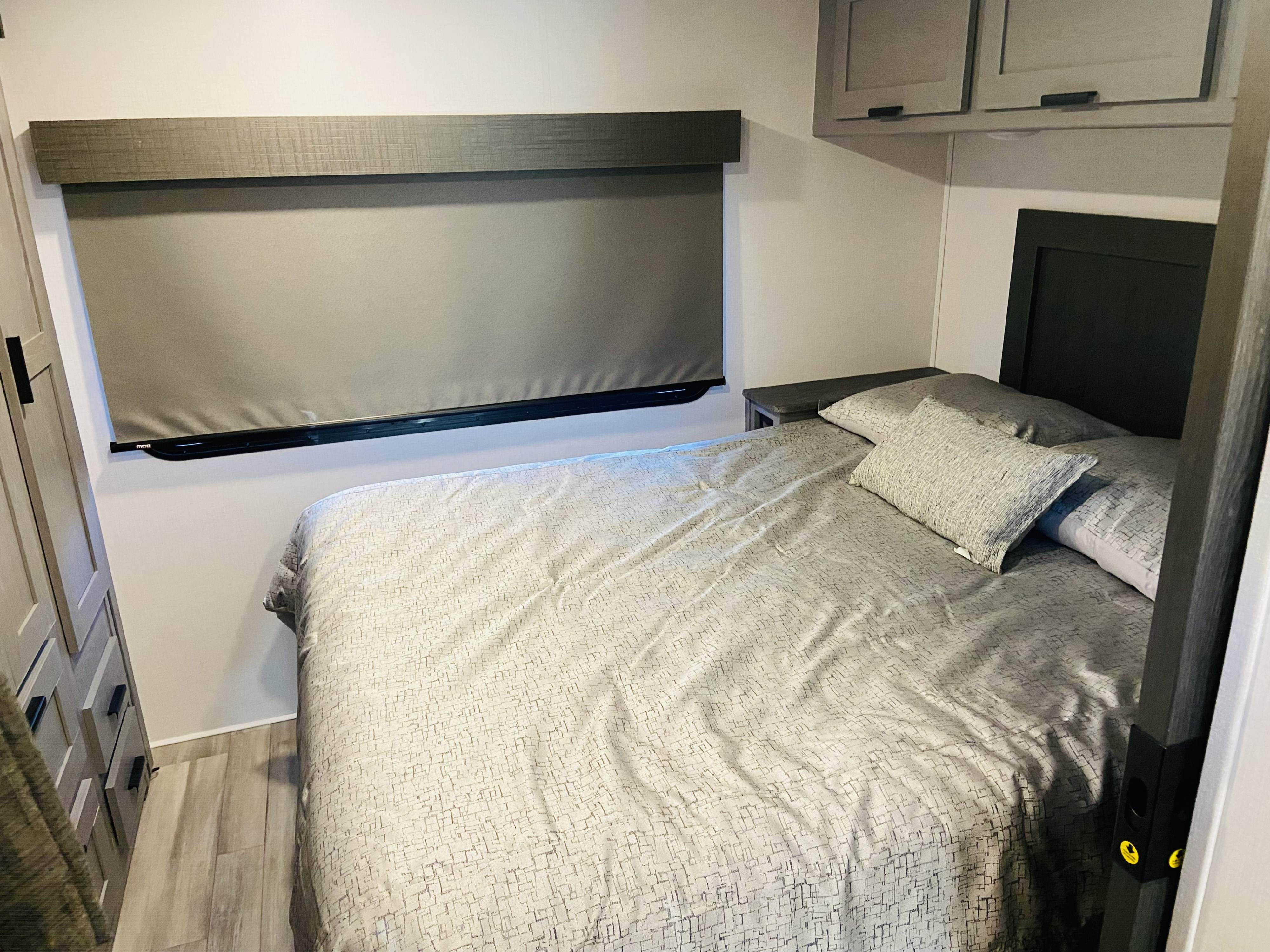 Comfortable and modern RV rental bedroom featuring a grey bed, nightstands, overhead storage, and a window blind.. Forest River Solera 2023