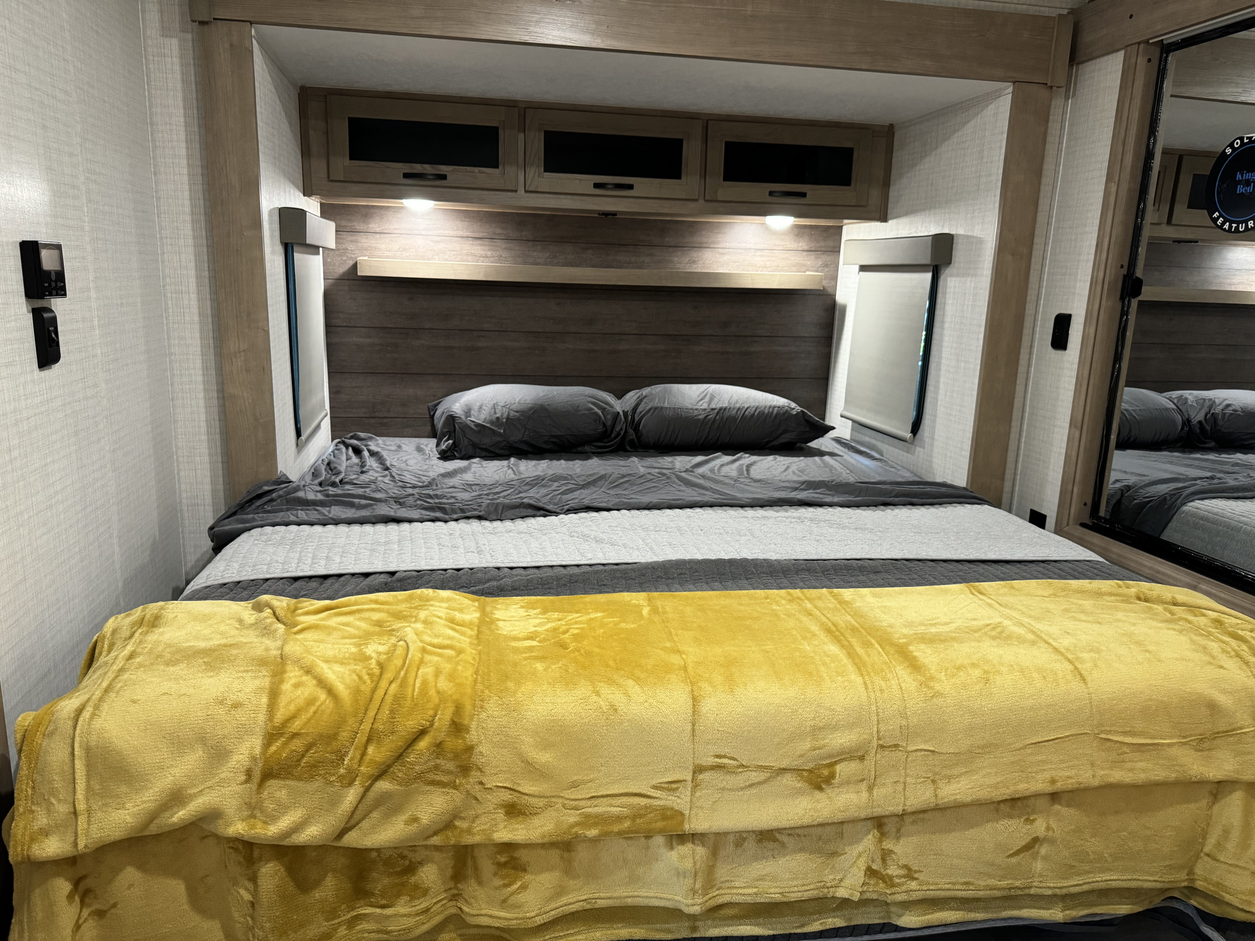 Comfortable RV rental bedroom with cozy bed, grey and yellow blankets, and overhead storage.. Palomino Solaire 2024