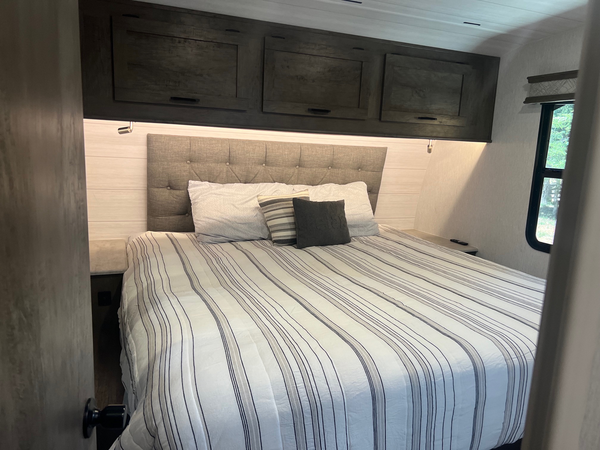 Experience comfort in this RV rental bedroom, featuring a neatly made bed, tufted headboard, and ample overhead storage.. Forest River Sandstorm 2022