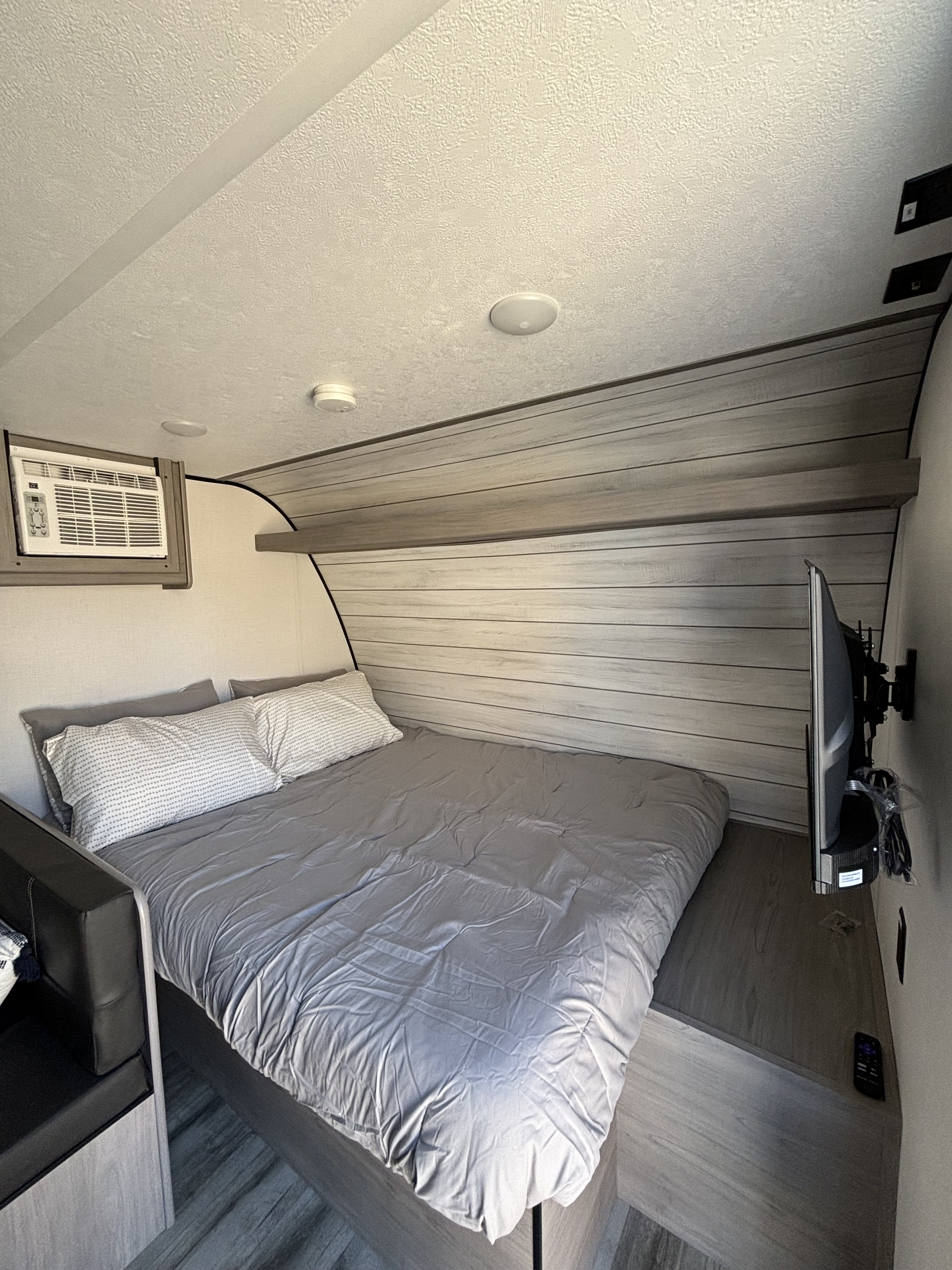 Cozy RV rental bedroom with grey-linened bed, wall-mounted AC unit, and TV. Ideal for a relaxing journey.. Coleman 17B 2024