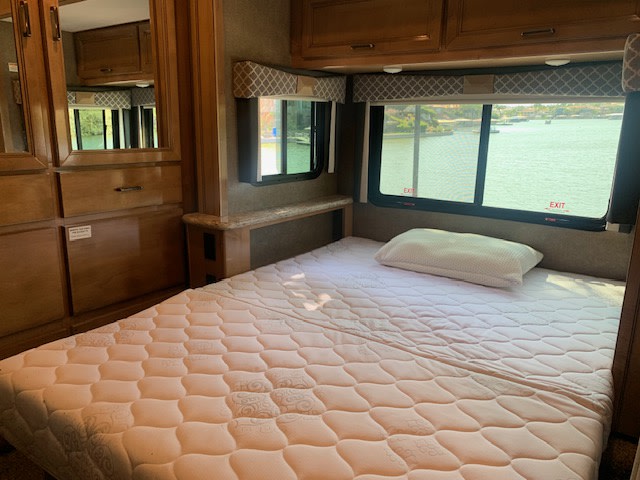 Interior of an RV rental showing a comfortable bed next to large windows with scenic water views.. Thor Quantum 2019