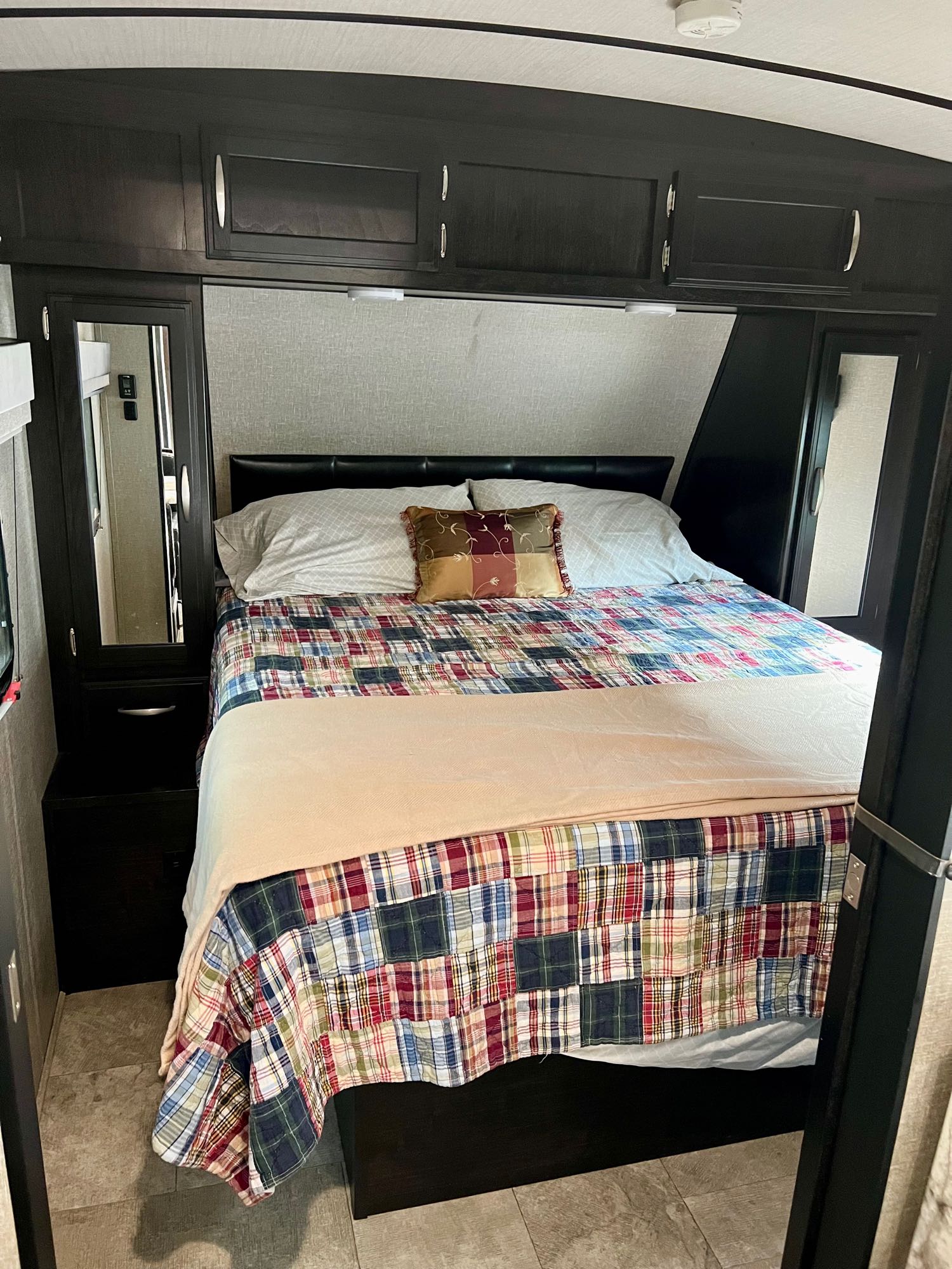 Inside an RV rental, a compact bedroom with a cozy bed, plaid quilt, dark cabinets, and mirrored closets. Perfect for adventurers.. Grand Design Imagine 2020