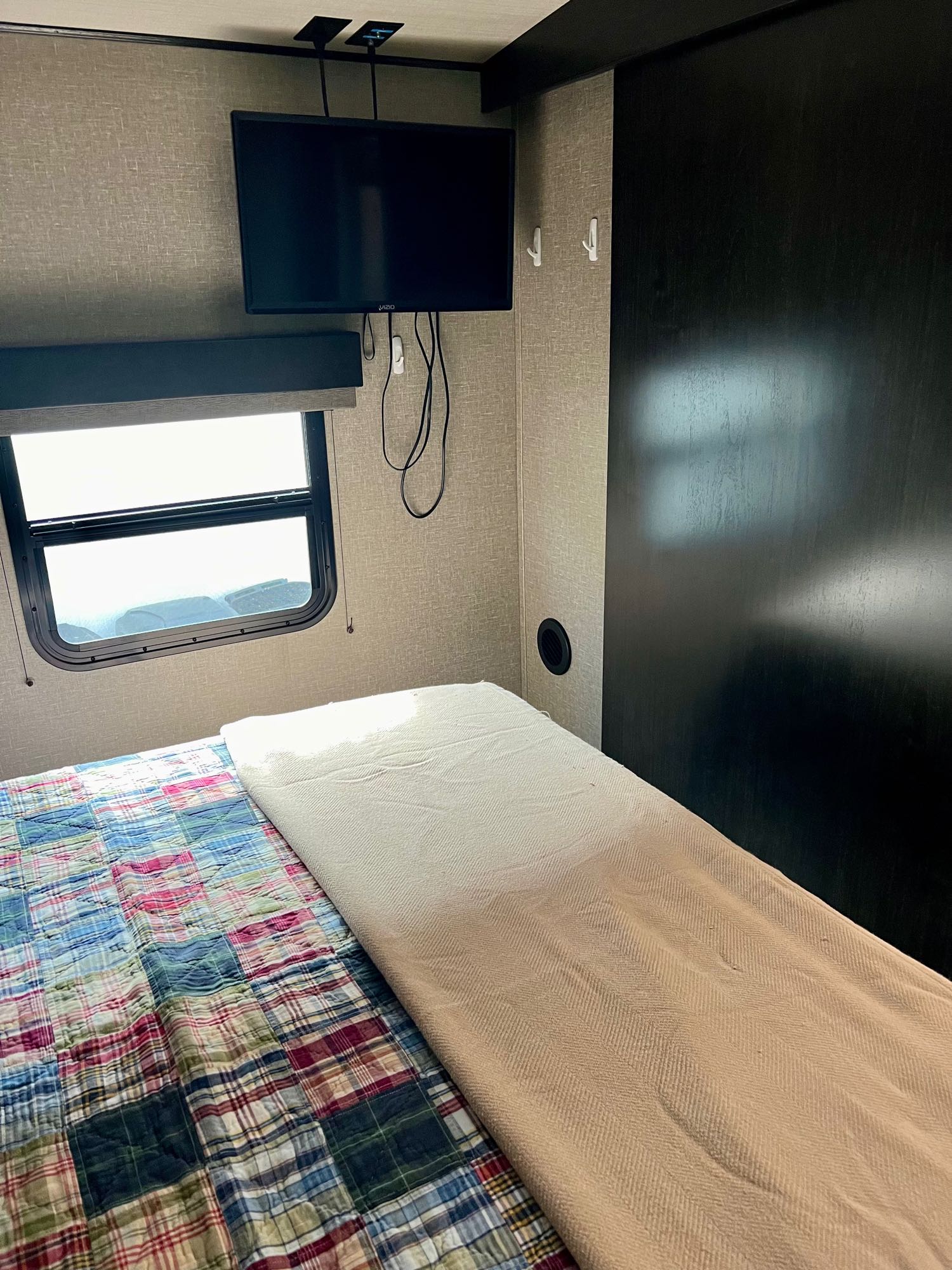 RV rental bedroom interior: compact space with a wall-mounted TV, window, and a bed with a colorful plaid quilt.. Grand Design Imagine 2020
