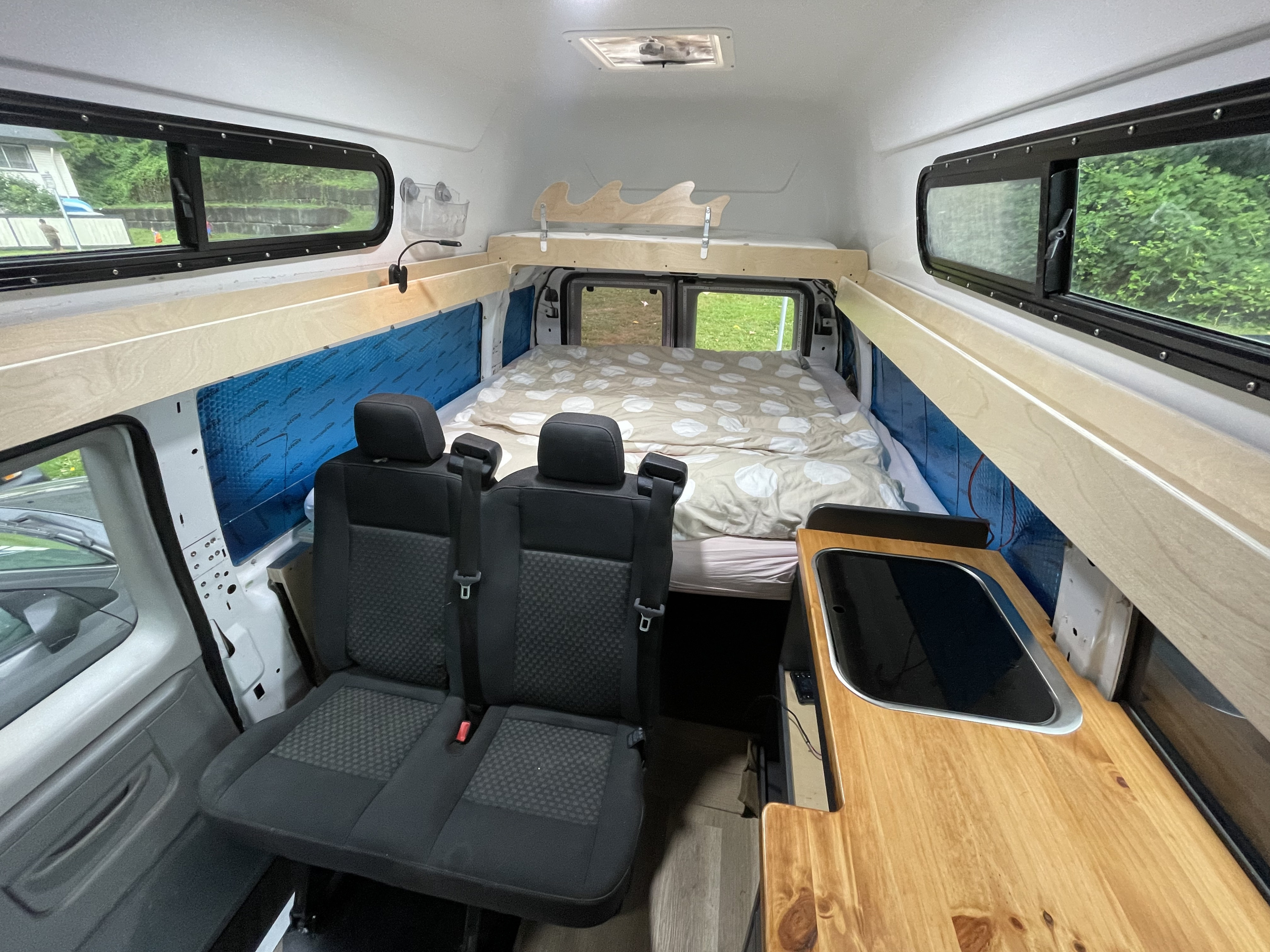 Cozy RV rental interior with bed, passenger seats, and kitchen. Perfect for camper van adventures.. Ford Econoline 2003