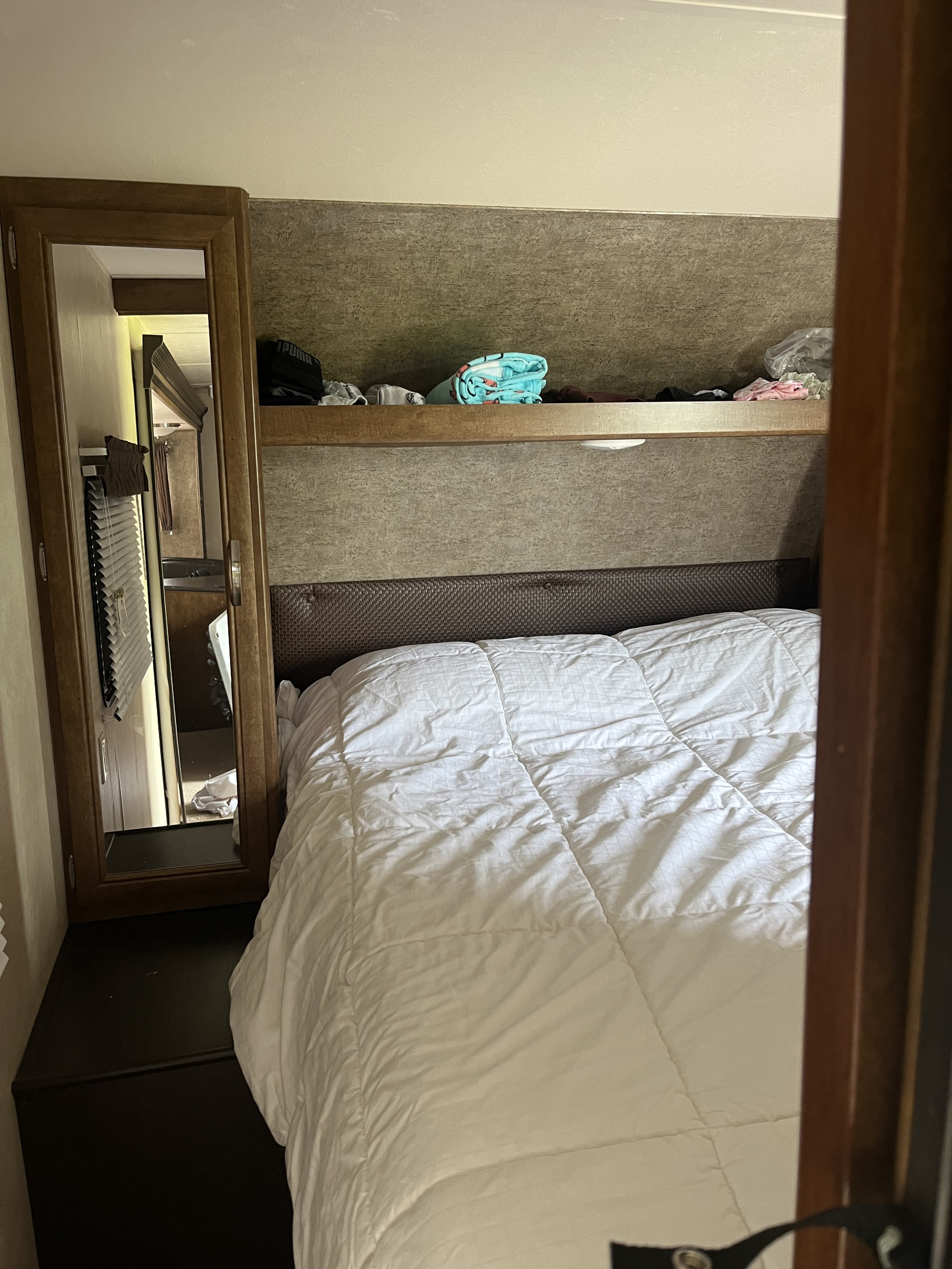 Inside an RV rental, a compact bedroom features a bed with white comforter, built-in storage, and mirrored cabinet.. Forest River Salem 2017