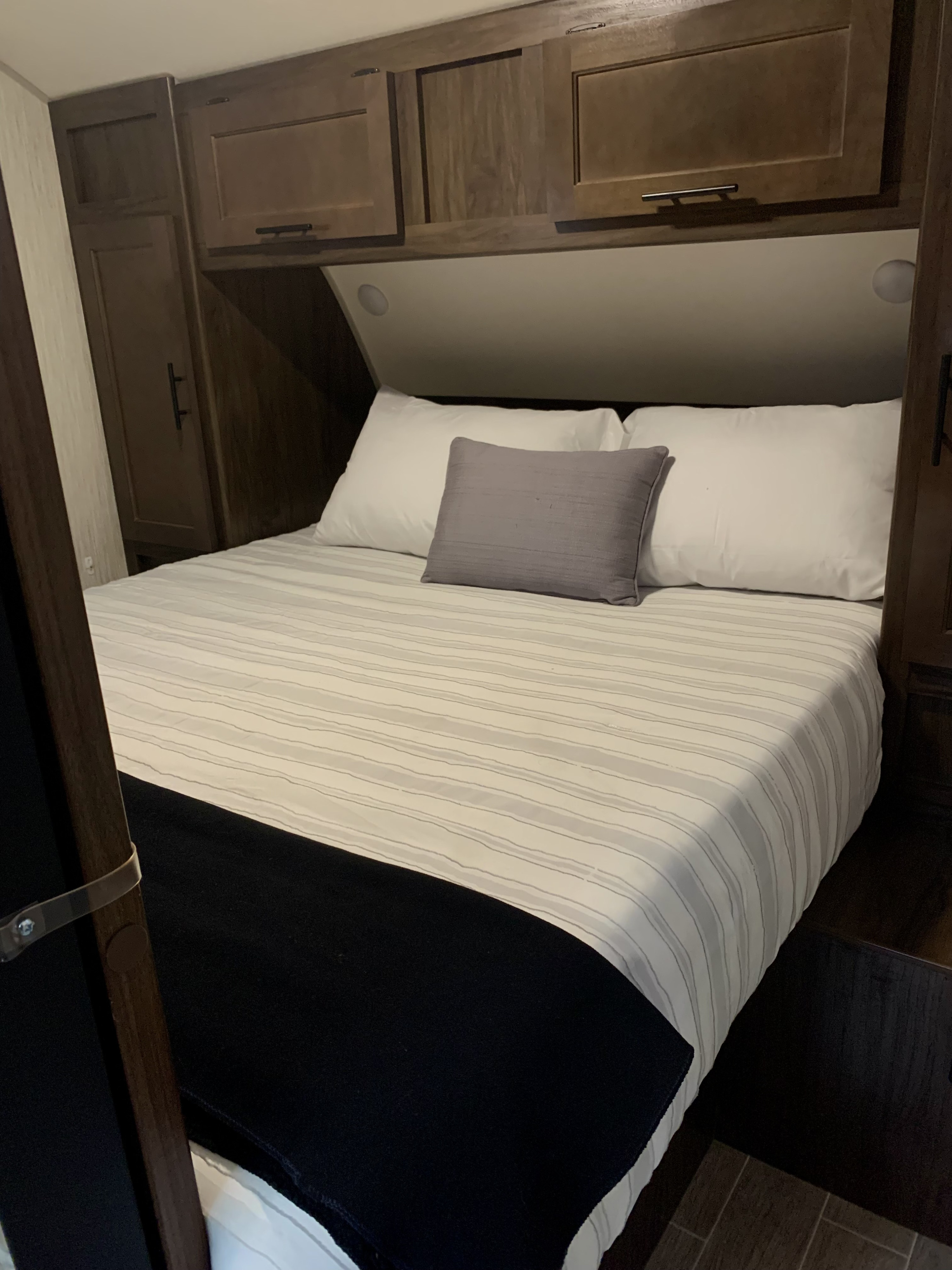 Compact RV rental bedroom with striped bedding, white pillows, and dark wood overhead cabinets for a cozy stay.. Forest River Cherokee Grey Wolf 2021