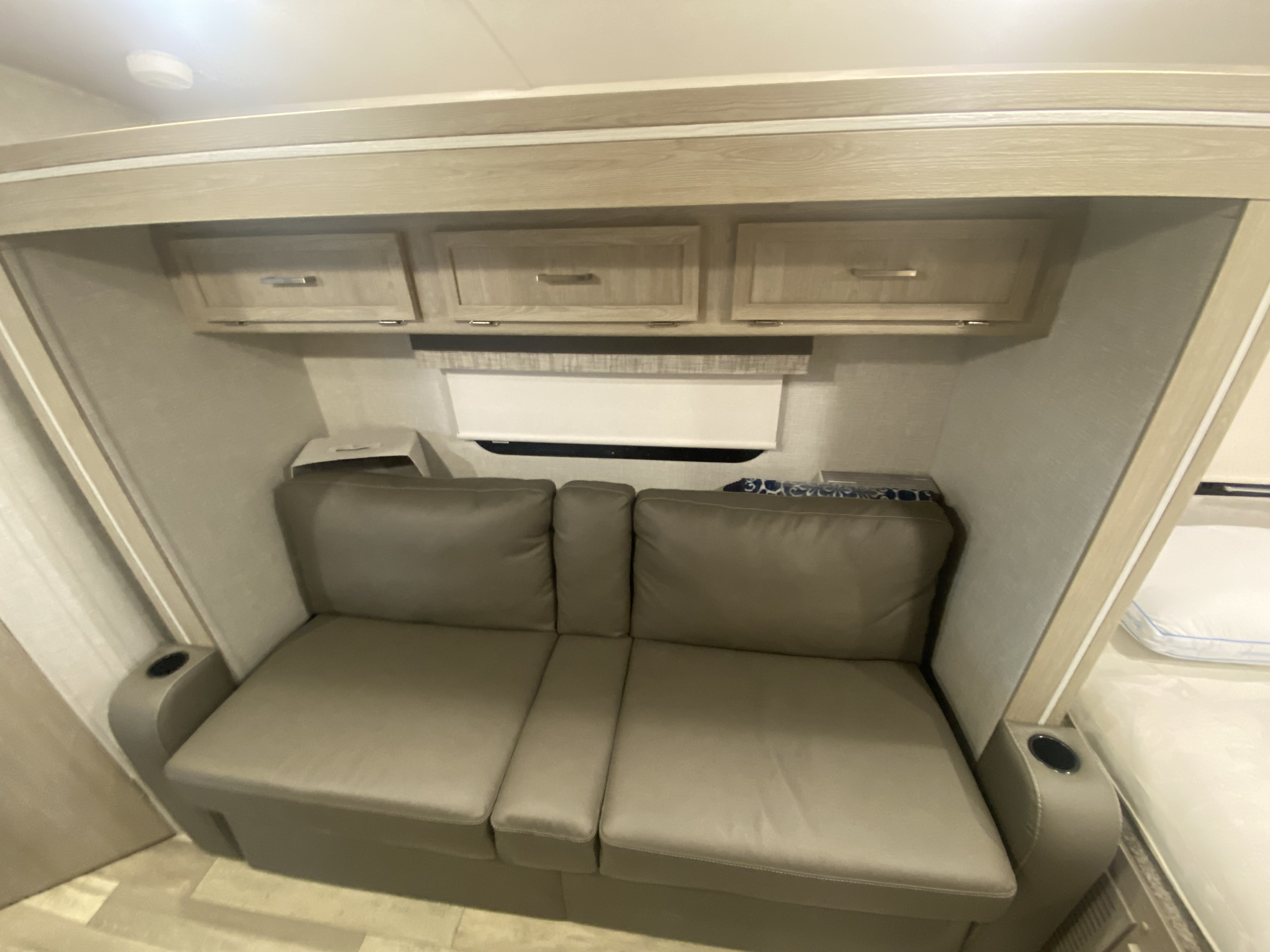 RV rental interior: Beige theater seating sofa with cupholders, under overhead cabinets & window. Ideal for compact living.. Forest River Flagstaff E-Pro 2022