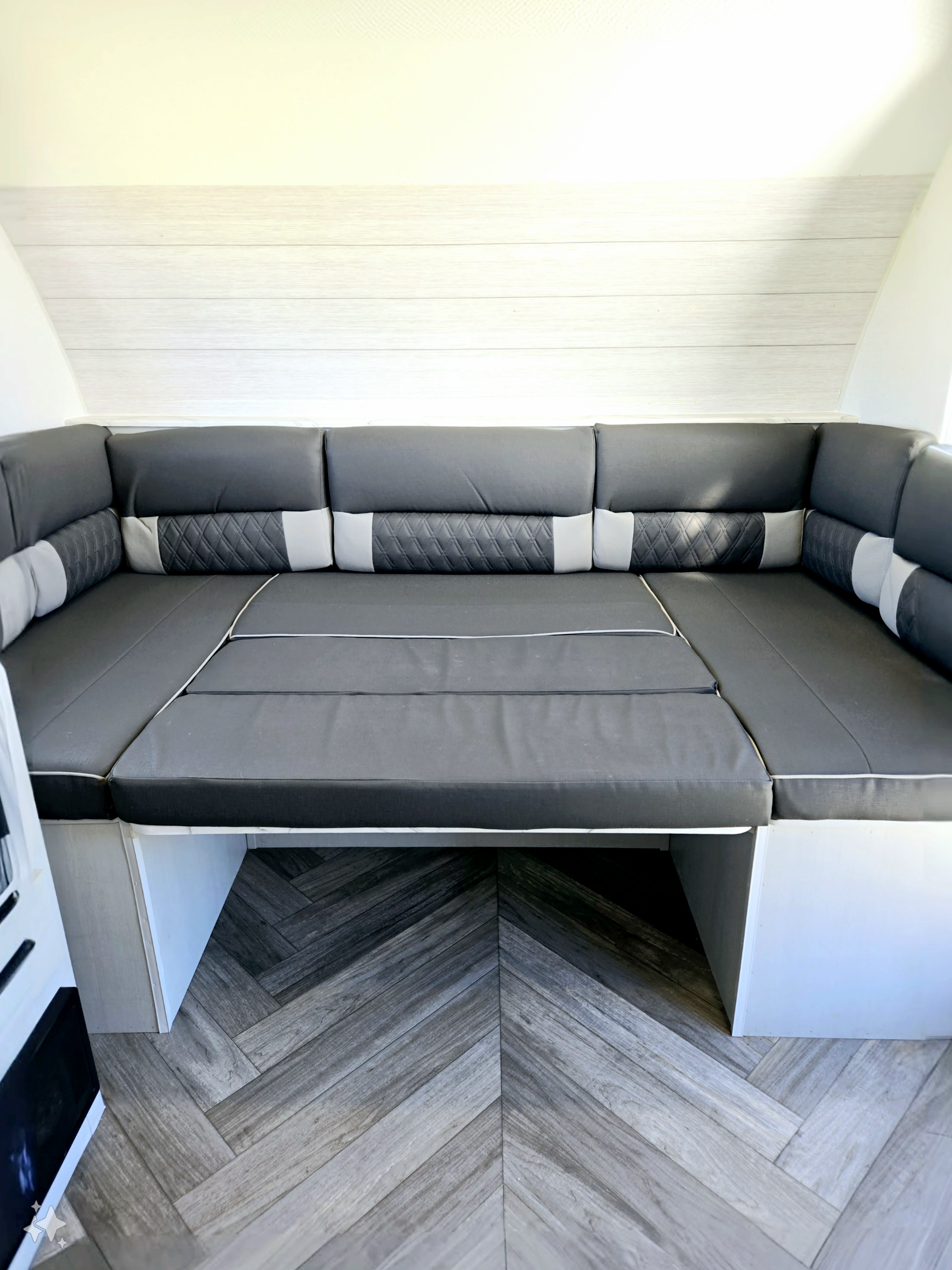 RV rental interior features versatile grey U-shaped seating with accent pillows, convertible into a bed, and a stylish herringbone floor.. Forest River Wildwood FSX 2022