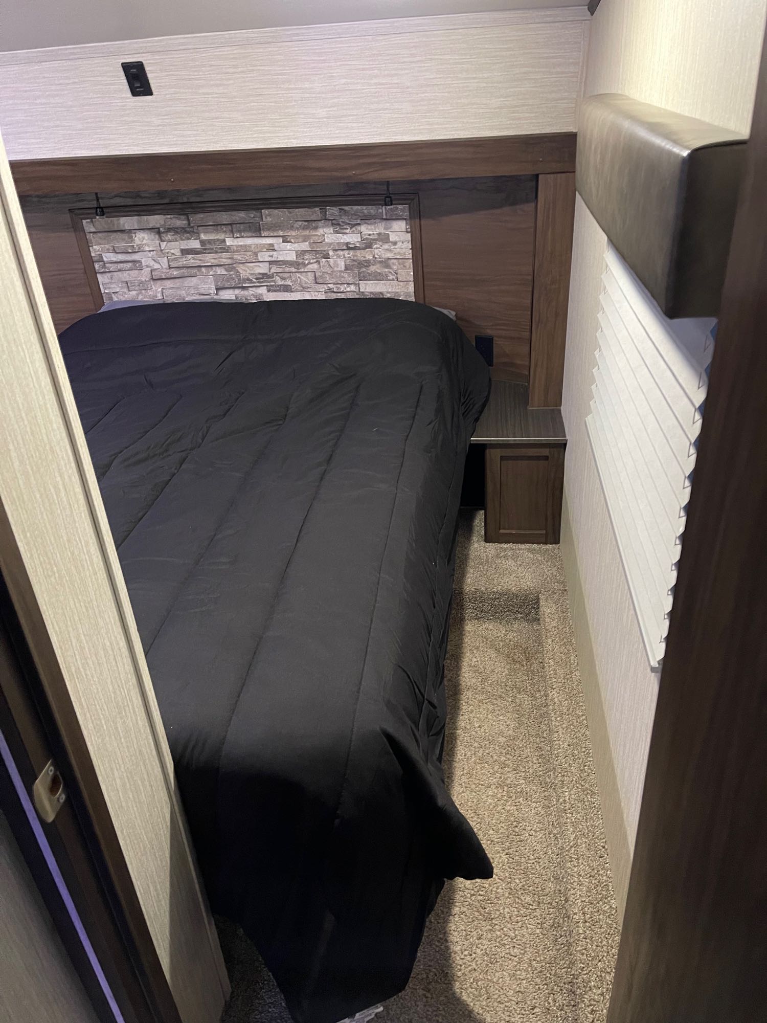 Cozy RV rental bedroom with a black comforter, stone headboard, and compact layout, ideal for travel adventures.. Forest River Cherokee Arctic Wolf 2019