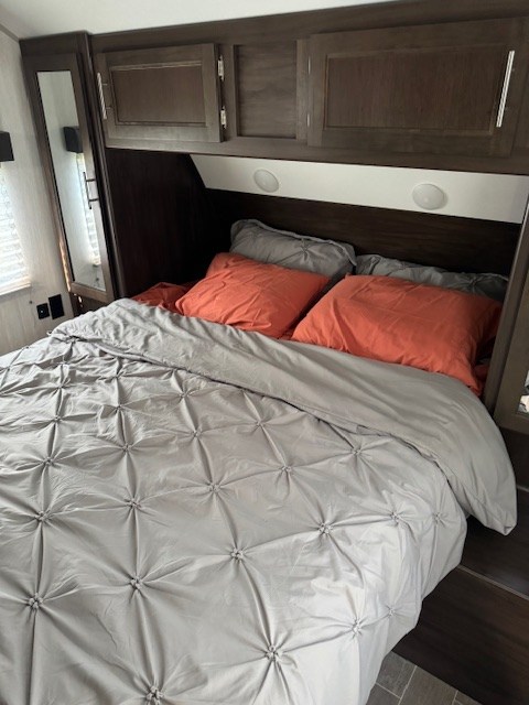 RV rental's inviting bedroom features a comfortable bed with a gray comforter, orange pillows, and overhead cabinets.. Forest River Cherokee Grey Wolf 2020