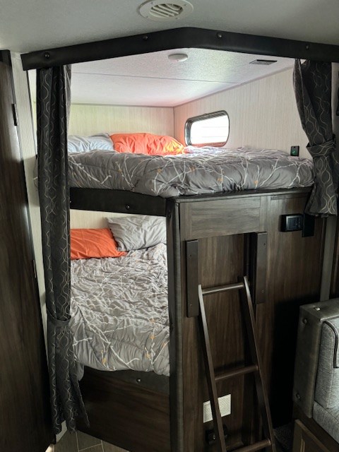 RV rental: A cozy bunk bed setup inside, featuring two beds with grey bedding, a window on the top bunk, and a wooden ladder.. Forest River Cherokee Grey Wolf 2020