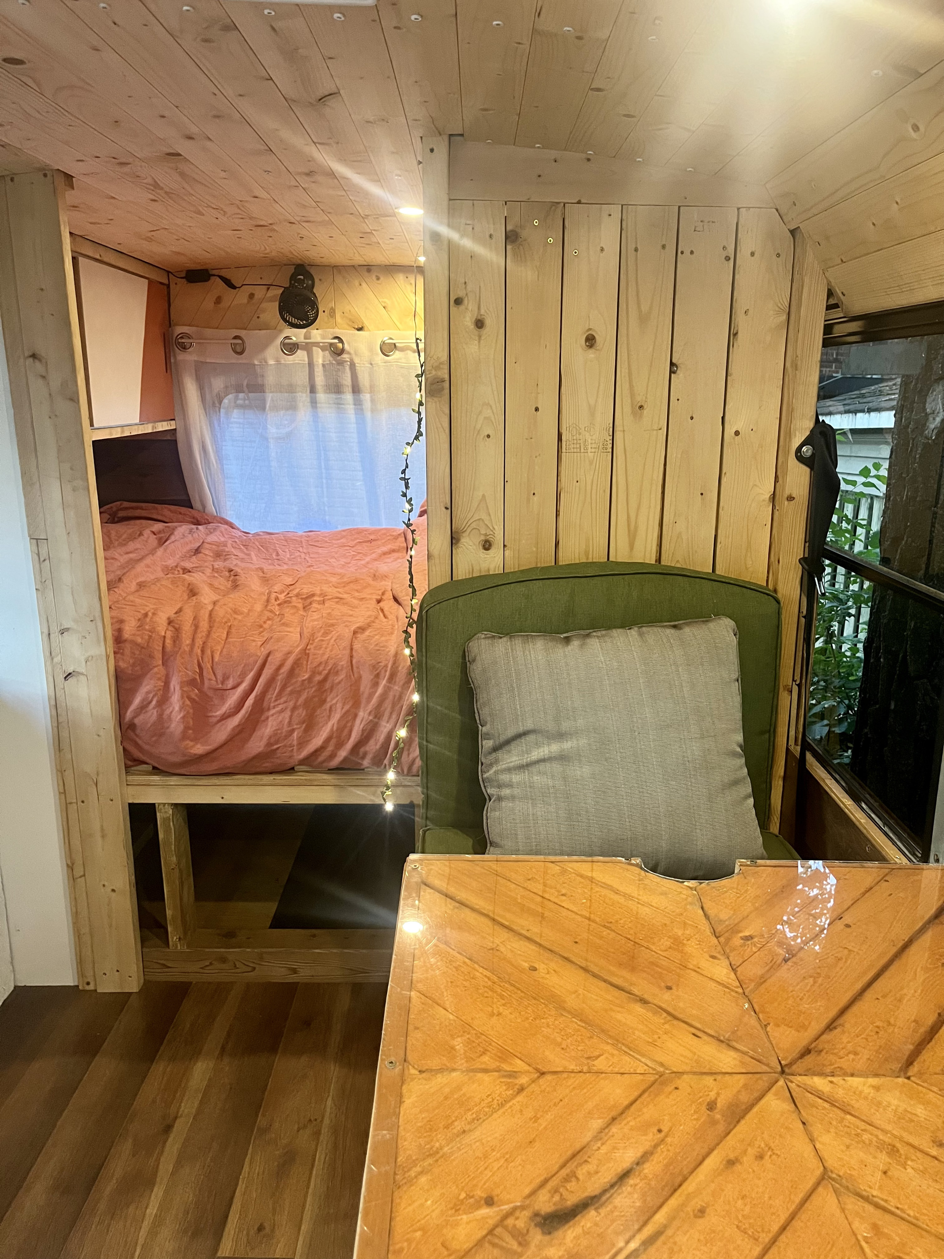 Inviting RV rental interior: wood-paneled bedroom with coral bedding, string lights, and a cozy green chair with wooden table.. Chevrolet Express 3500 2009