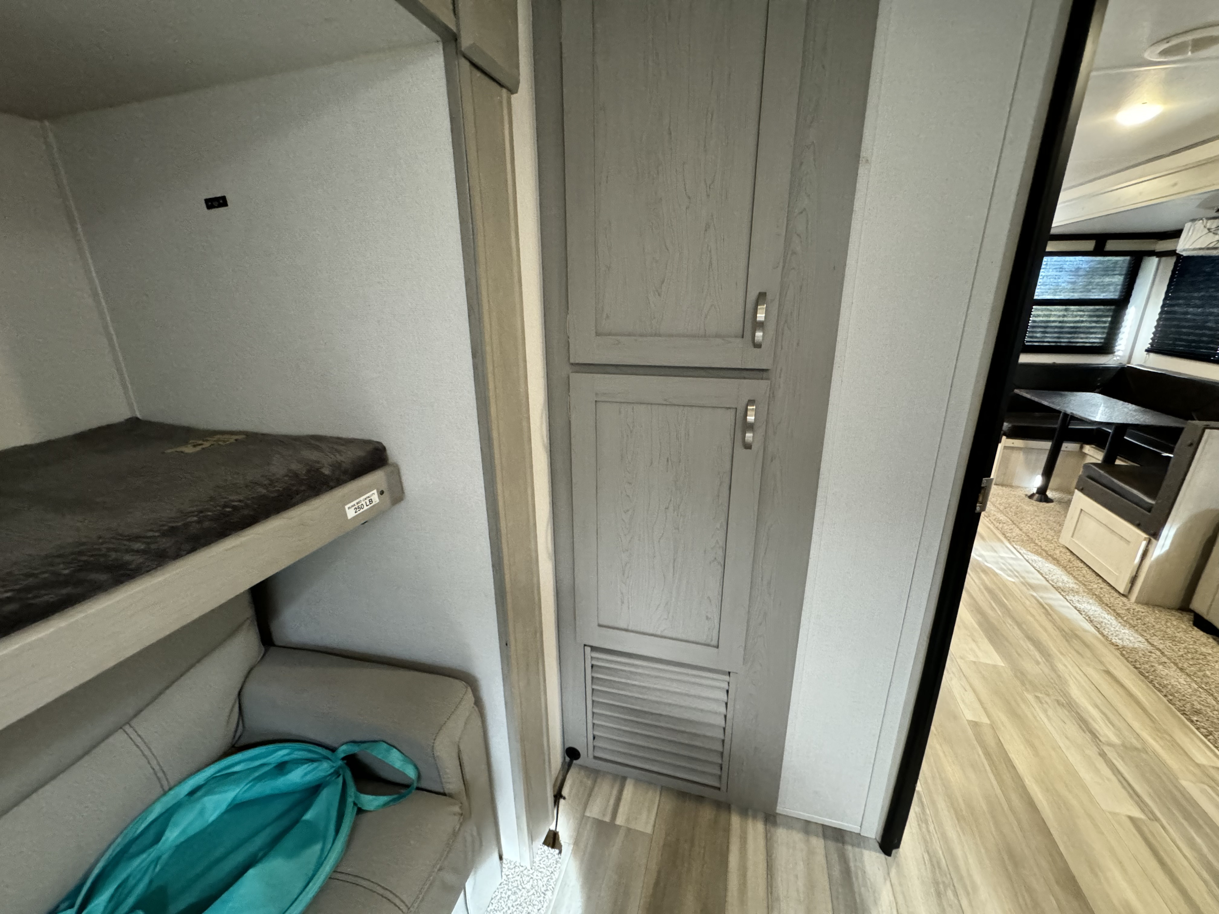 RV rental interior features bunk beds, a tall gray storage cabinet, and a glimpse of the dinette area with windows.. Prime Time Lacrosse 2022