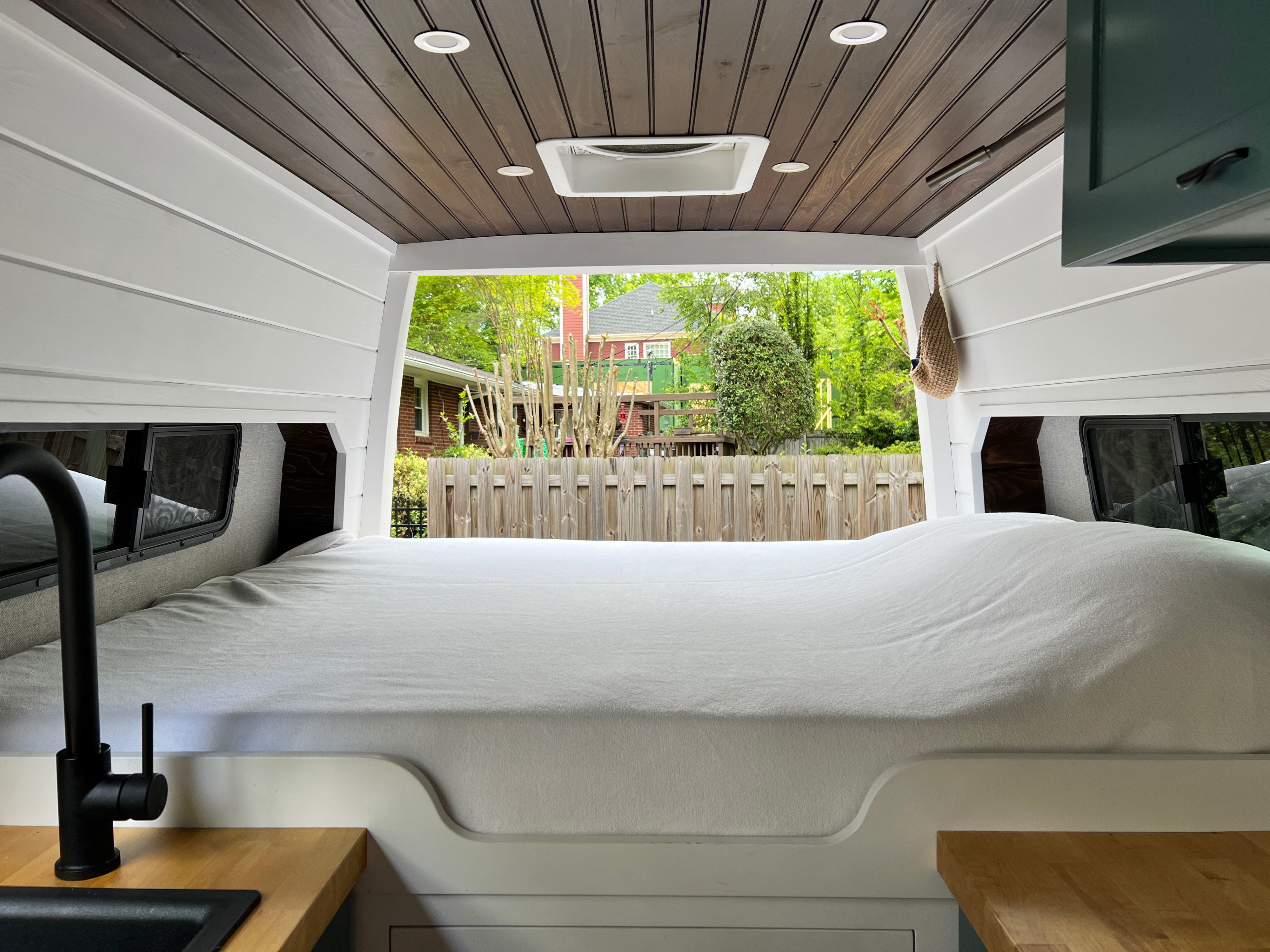 Inside this RV rental: a modern camper van with wood ceiling, cozy bed, and outdoor view from the rear.. Mercedes Sprinter 2020