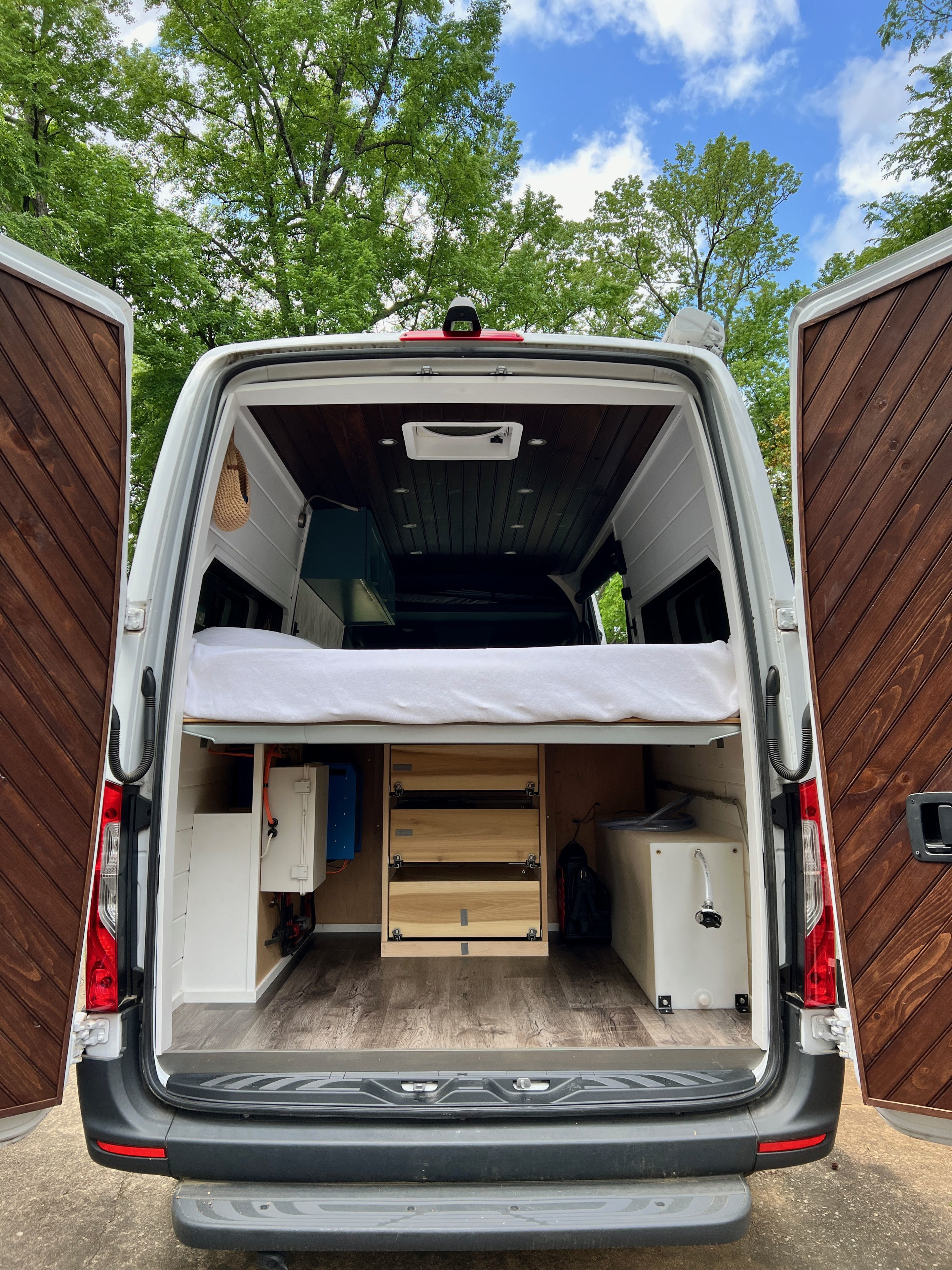 Rear interior of a customized camper van, showcasing a bed, storage, and water tank—perfect for your next RV rental.. Mercedes Sprinter 2020