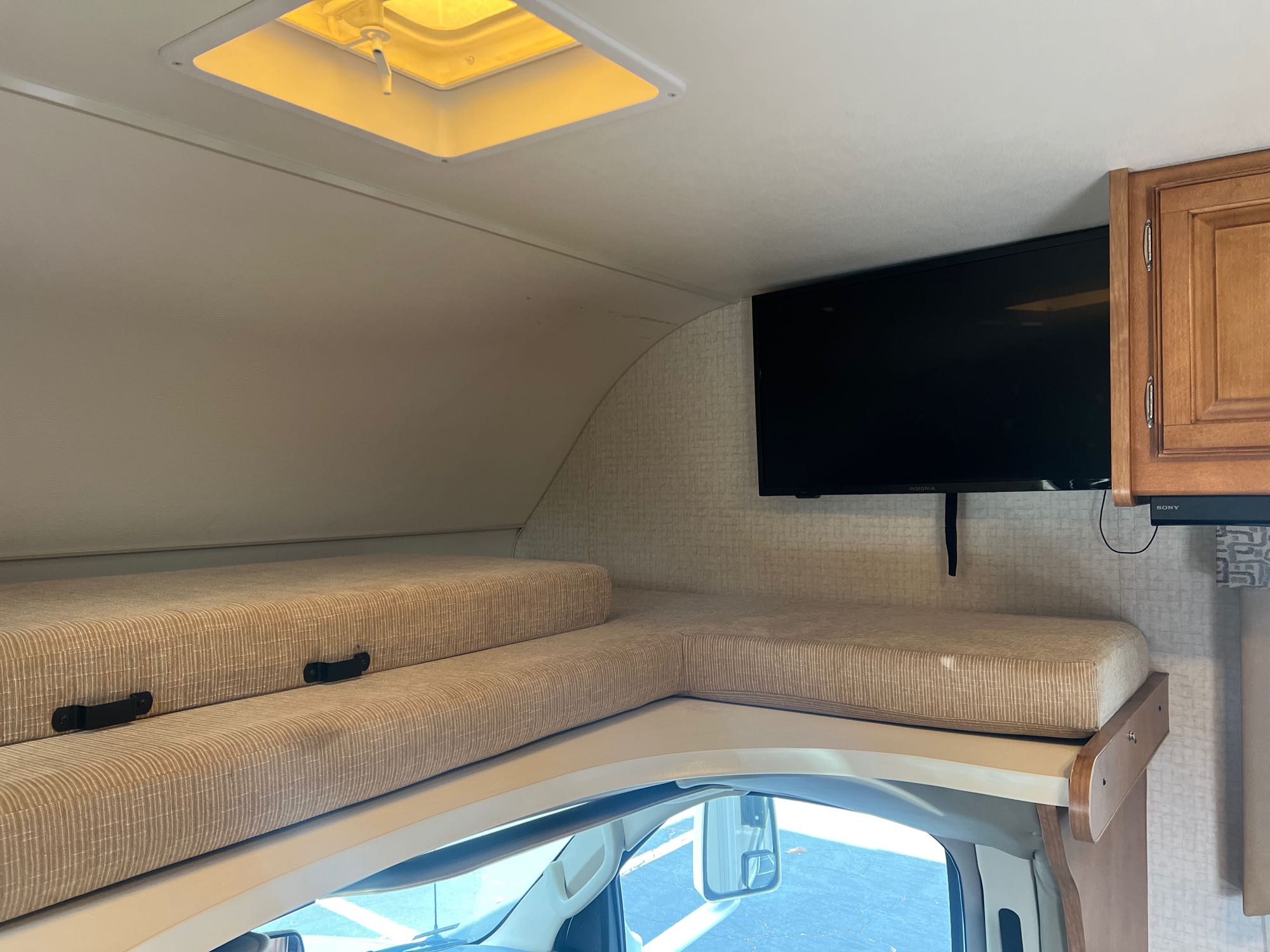 RV rental interior showing the over-cab bunk bed with cushions, a wall-mounted TV, and a ceiling vent.. Winnebago Minnie Winnie 2017