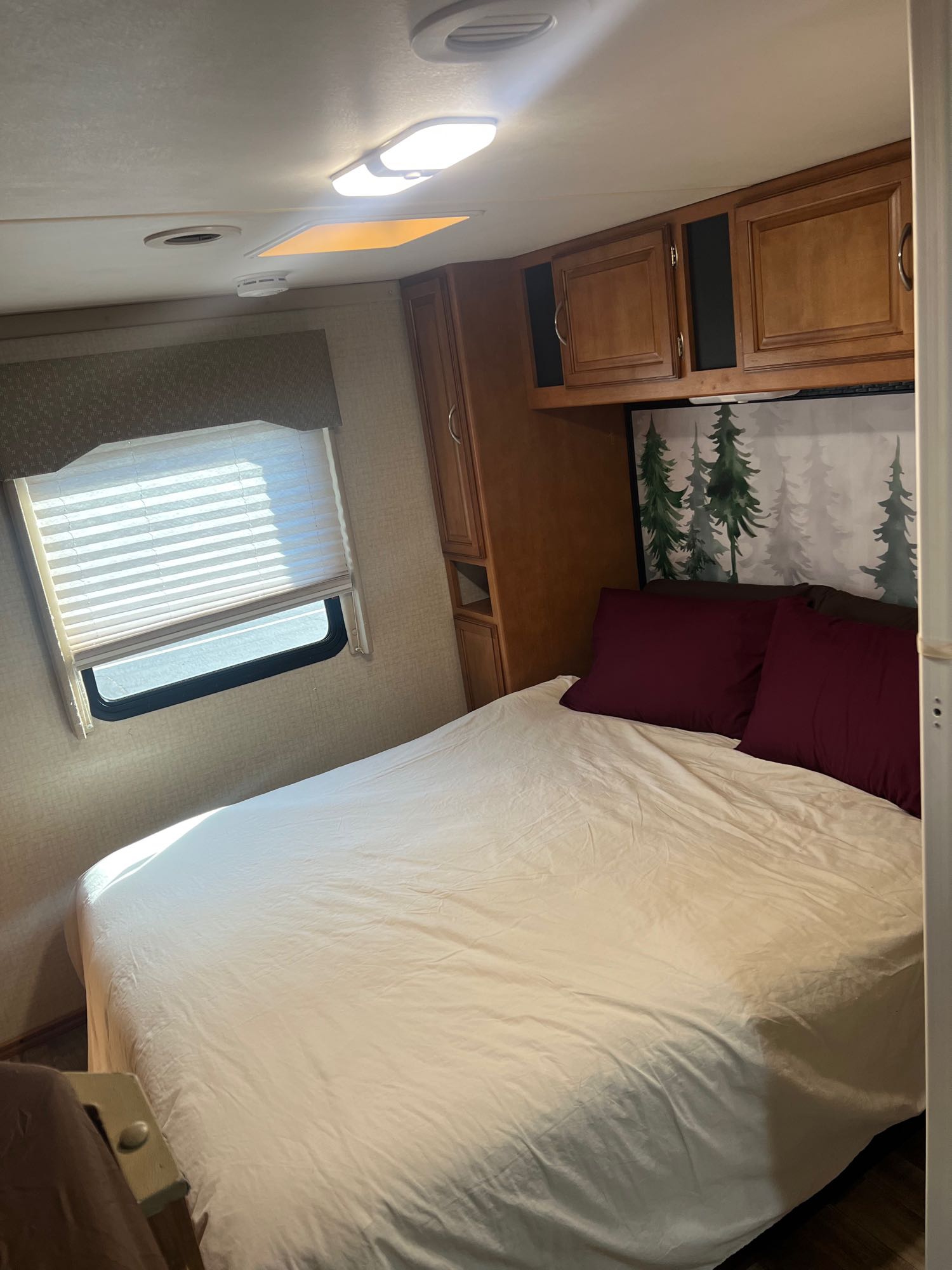 Cozy RV rental bedroom featuring a comfortable bed, window with blinds, overhead cabinets, and a nature-themed headboard.. Winnebago Minnie Winnie 2017