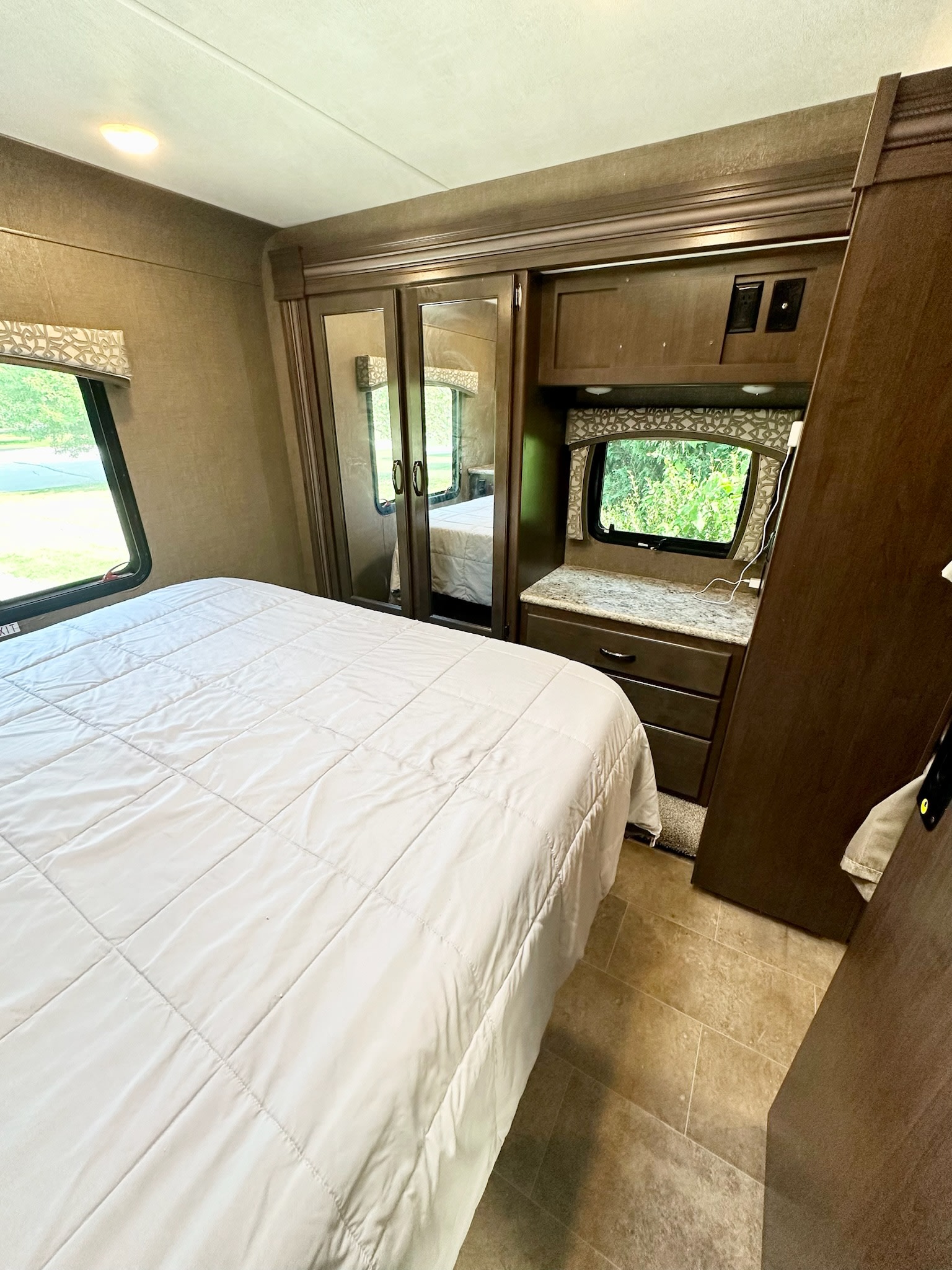 RV rental bedroom with a white bed, mirrored wardrobe, dresser, and scenic windows.. Thor Chateau 2019