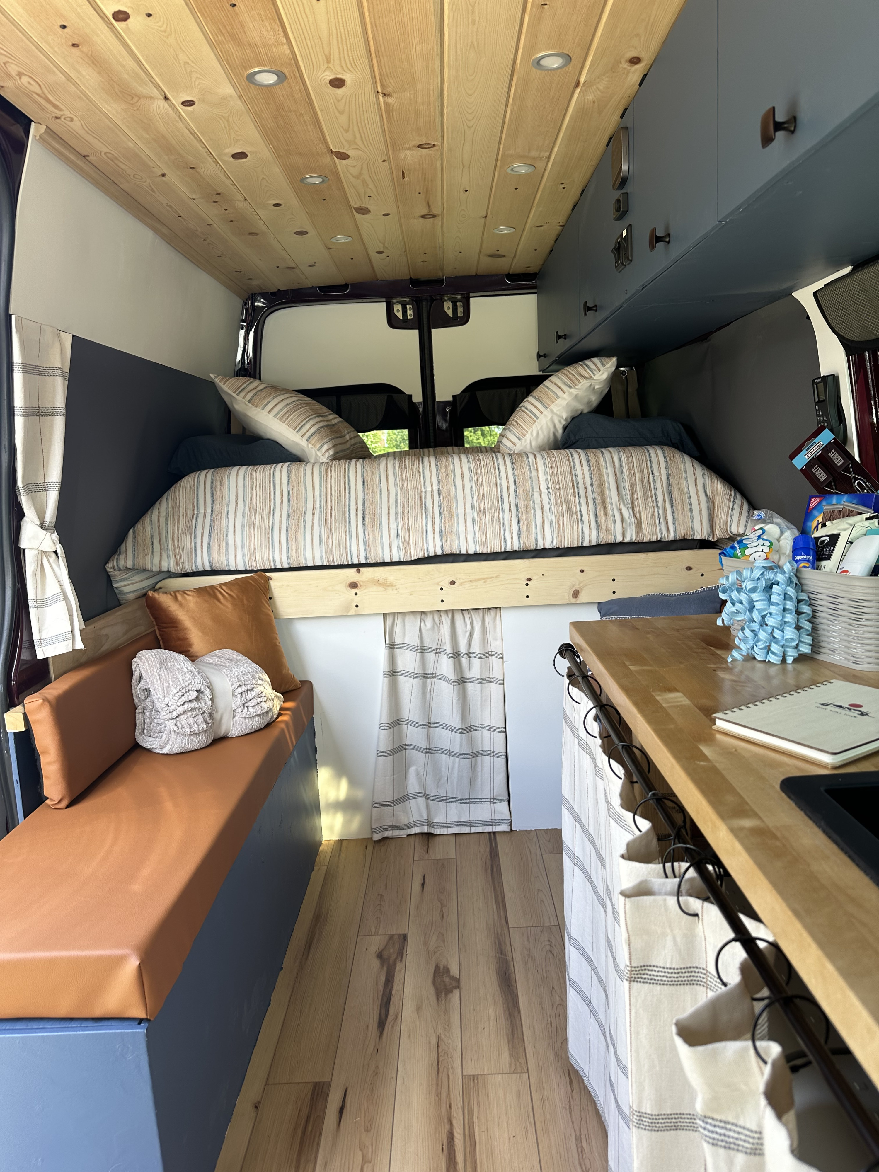 Cozy RV rental interior: wood-paneled ceiling, comfortable bed, compact kitchen, and seating area.. Dodge Sprinter Van 2008