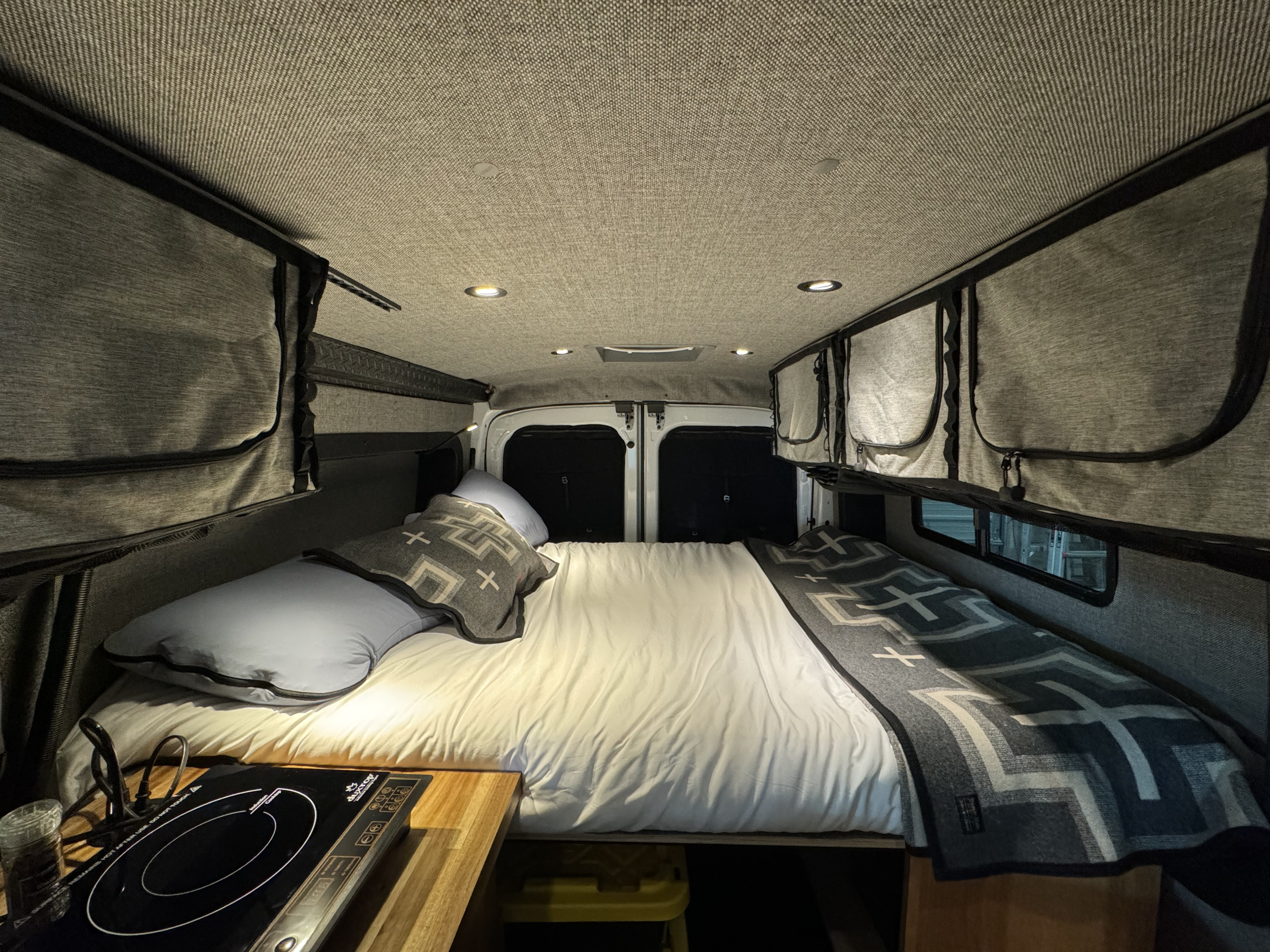 Cozy RV rental interior featuring a bed, ample storage, and a compact kitchen setup for comfortable travel.. Ford Transit Custom 2023