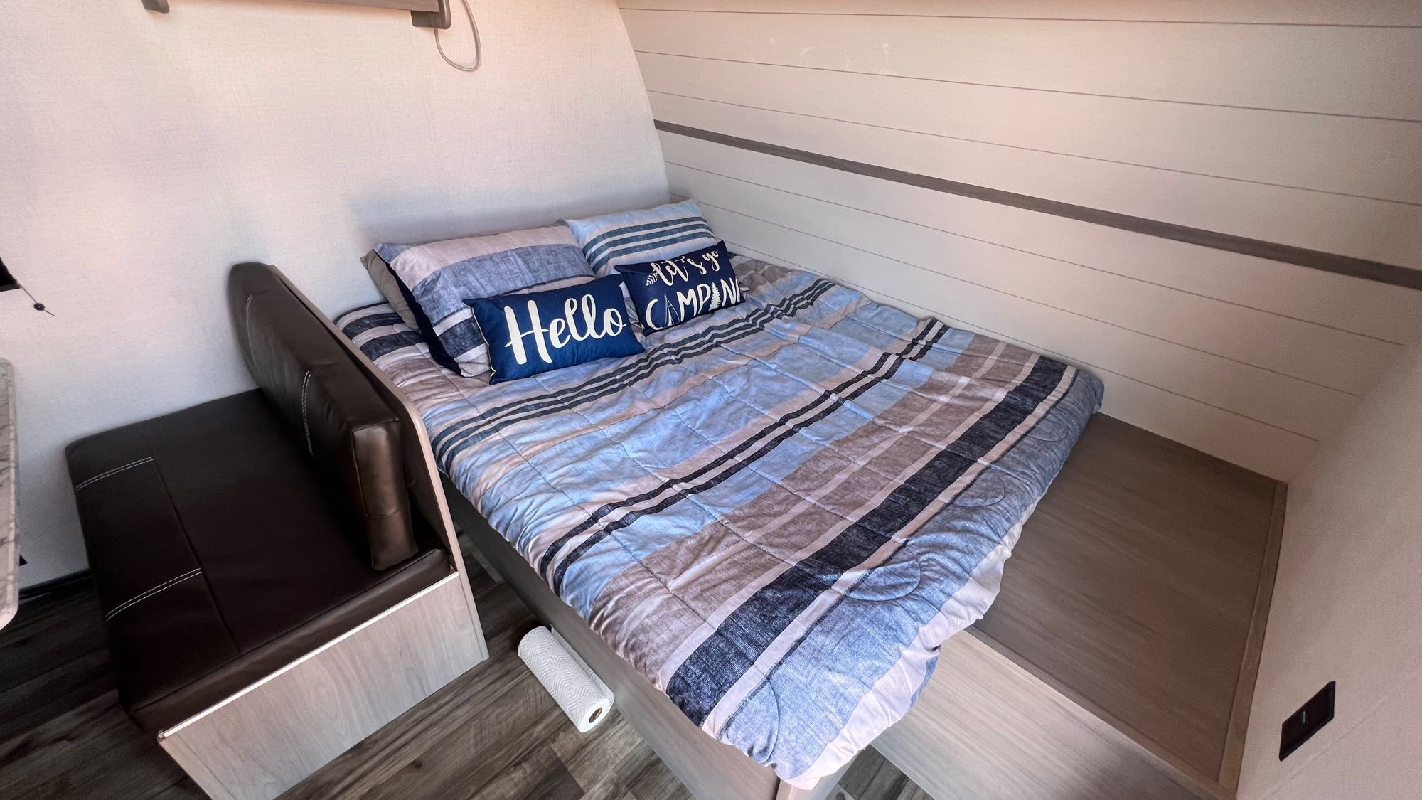 Cozy RV rental interior with a striped bed, "Hello" and "Let's Go Camping" pillows, and a dark brown bench.. Dutchmen Coleman Lantern LT 2024