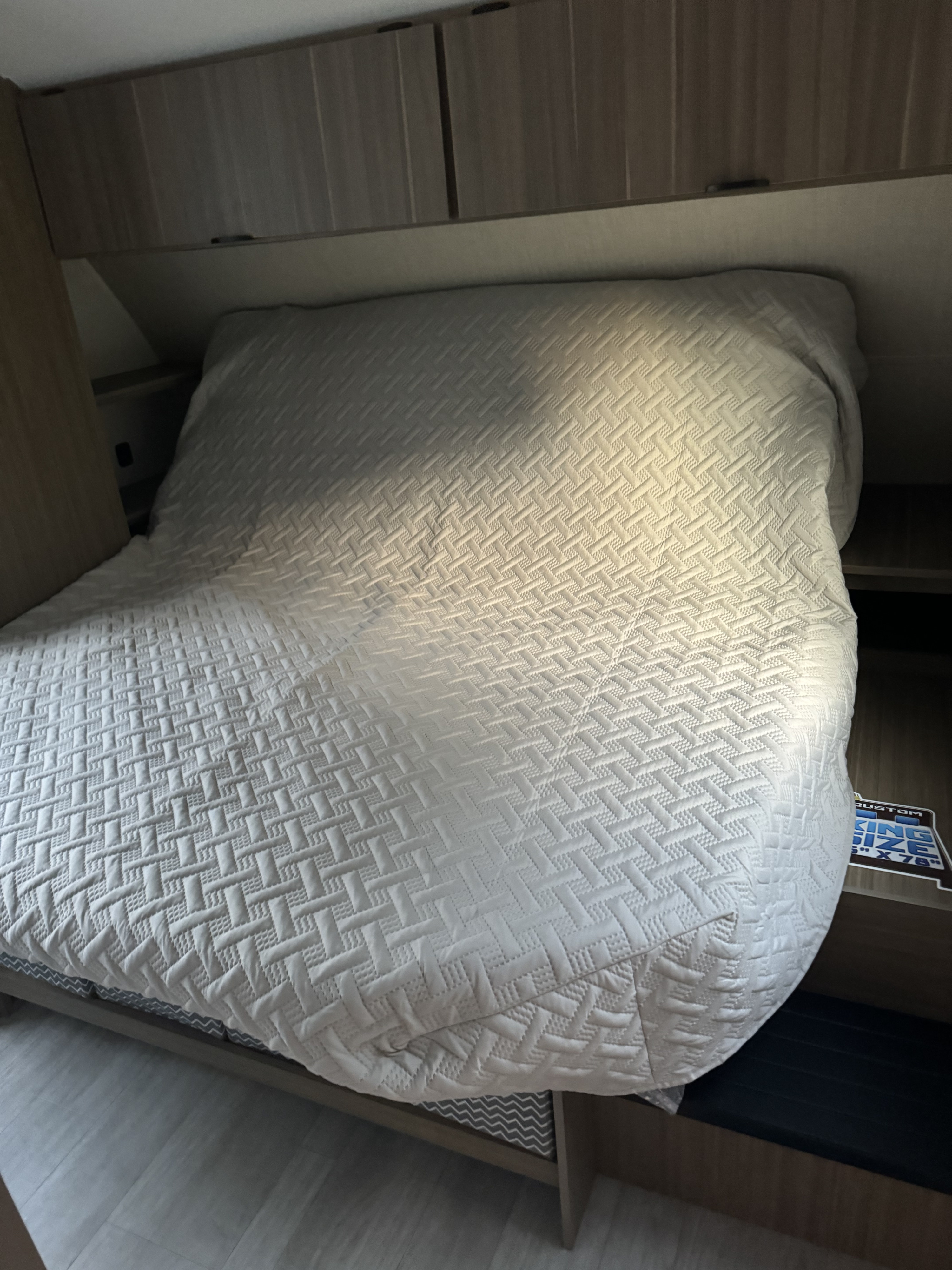 Inside an RV rental: a compact bedroom with a white quilted bed, overhead cabinets, and built-in storage.. Forest river Salem cruise lite 273qbxl 2025